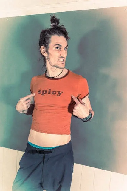 Person with messy hair pointing at a red shirt that says 'spicy' and making a silly face.
