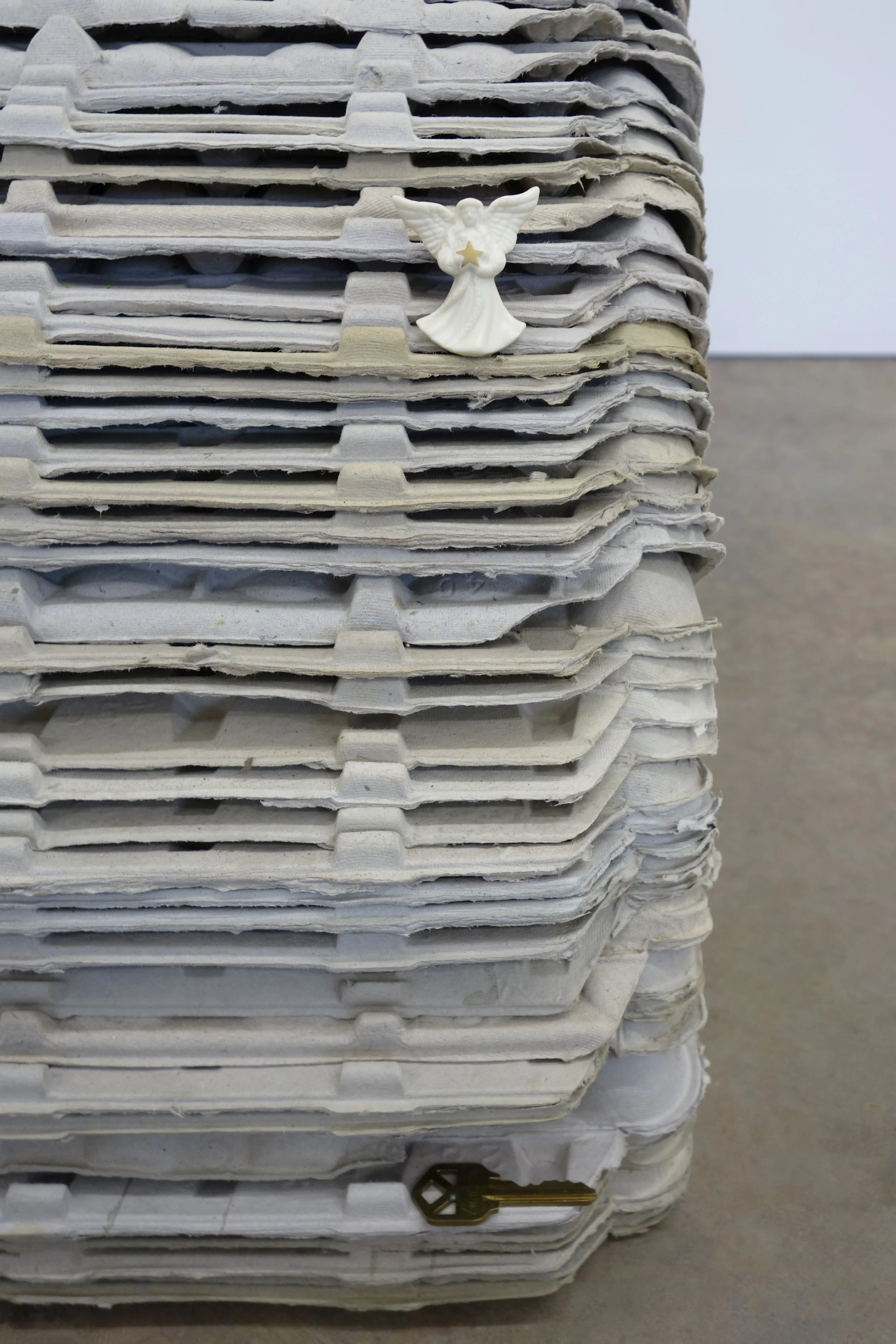   Investment , 2026. egg cartons, nail, cast and hand-painted epoxy resin, shell casing, yellow jacket and epoxy resin in bottle cap, sunglasses, angel pin, door key, and steel, 19 x 46 x 12 in (48.3 x 116.8 x 30.5 cm) 