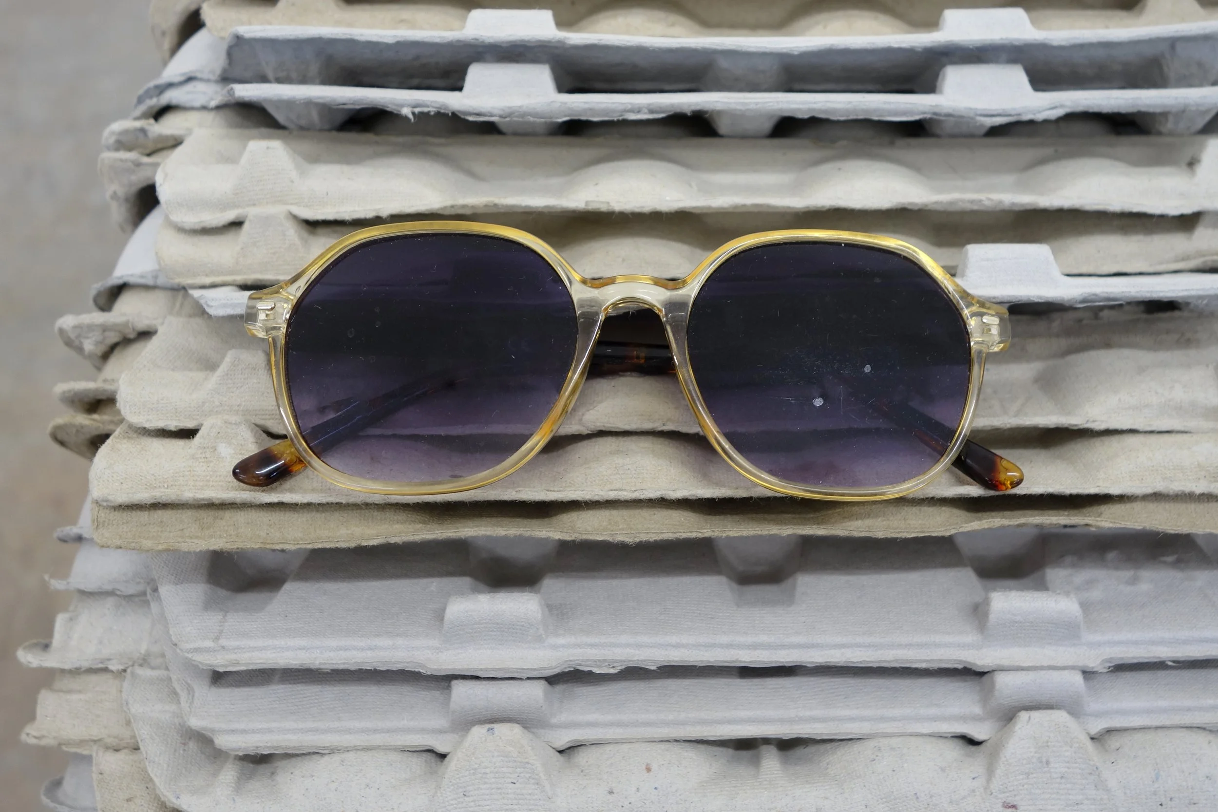   Investment , 2026. egg cartons, nail, cast and hand-painted epoxy resin, shell casing, yellow jacket and epoxy resin in bottle cap, sunglasses, angel pin, door key, and steel, 19 x 46 x 12 in (48.3 x 116.8 x 30.5 cm) 
