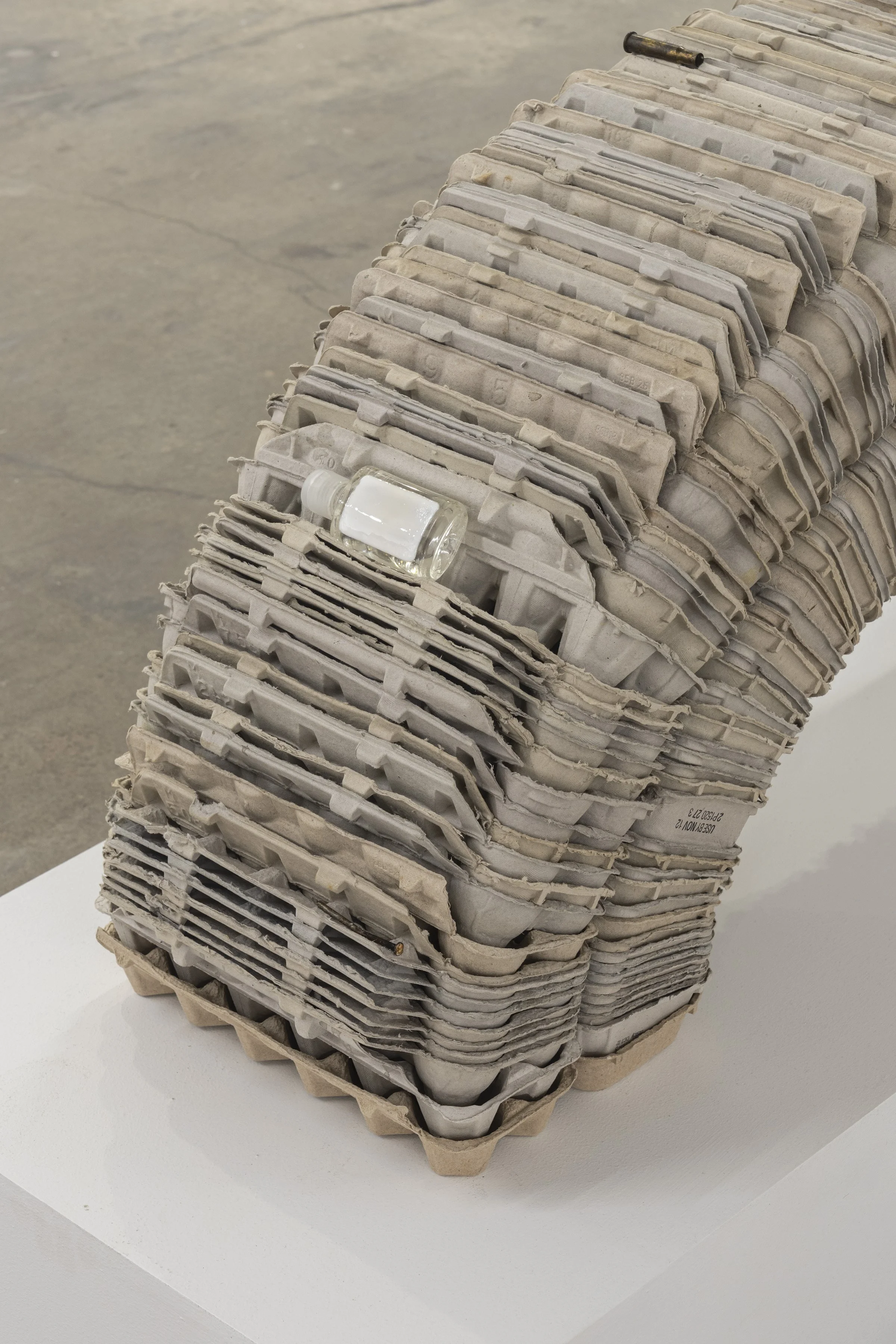   Investment , 2026, egg cartons, nail, cast and hand-painted epoxy resin, shell casing, yellow jacket and epoxy resin in bottle cap, sunglasses, angel pin, door key, and steel, 19 x 46 x 12 in (48.3 x 116.8 x 30.5 cm) 