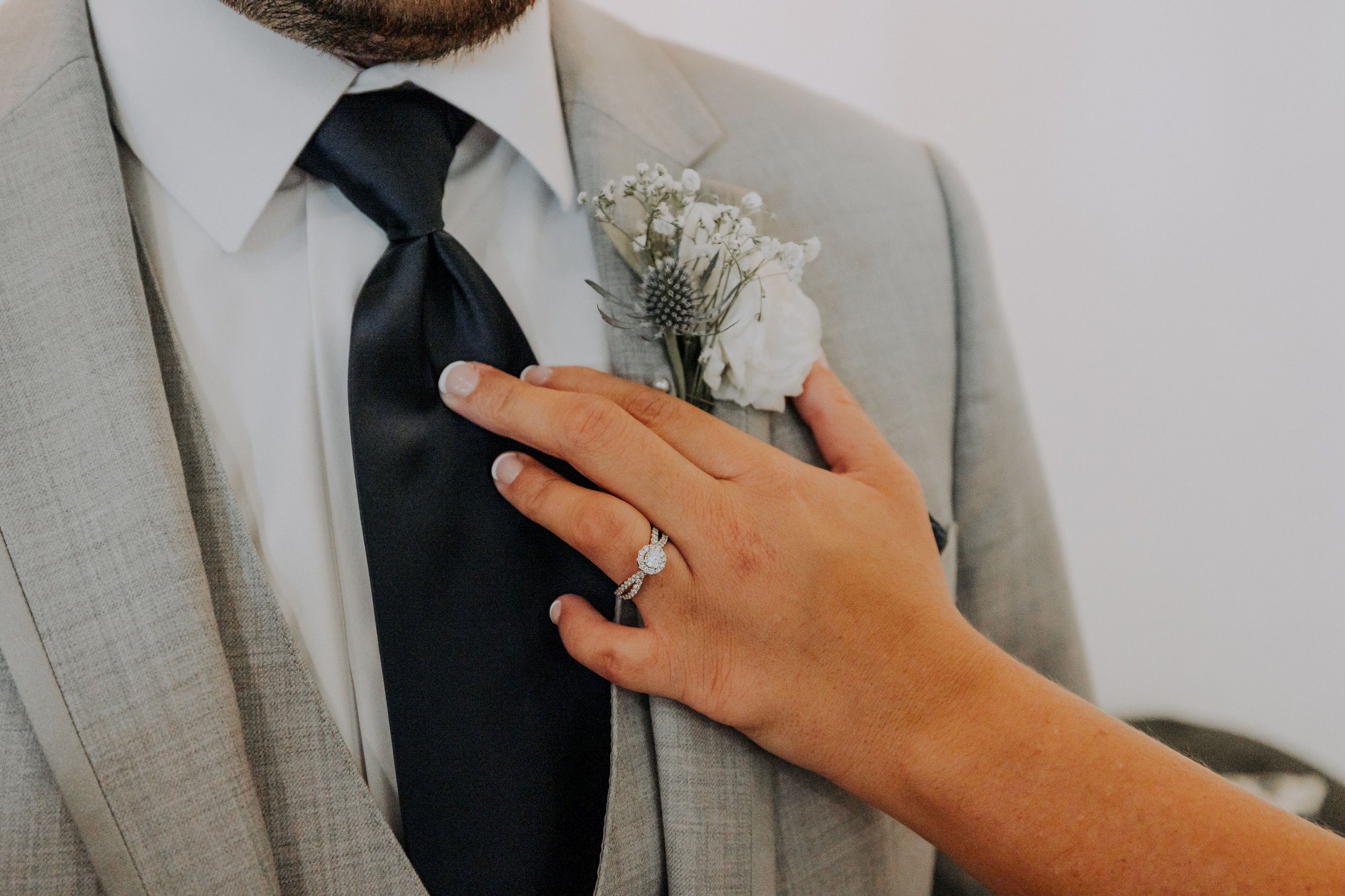 A woman with a wedding ring places her hand over a man's chest, he wears a tuxedo and boutonniere on the elegant patio outside of the Revel Center in Grand Rapids, Michigan.