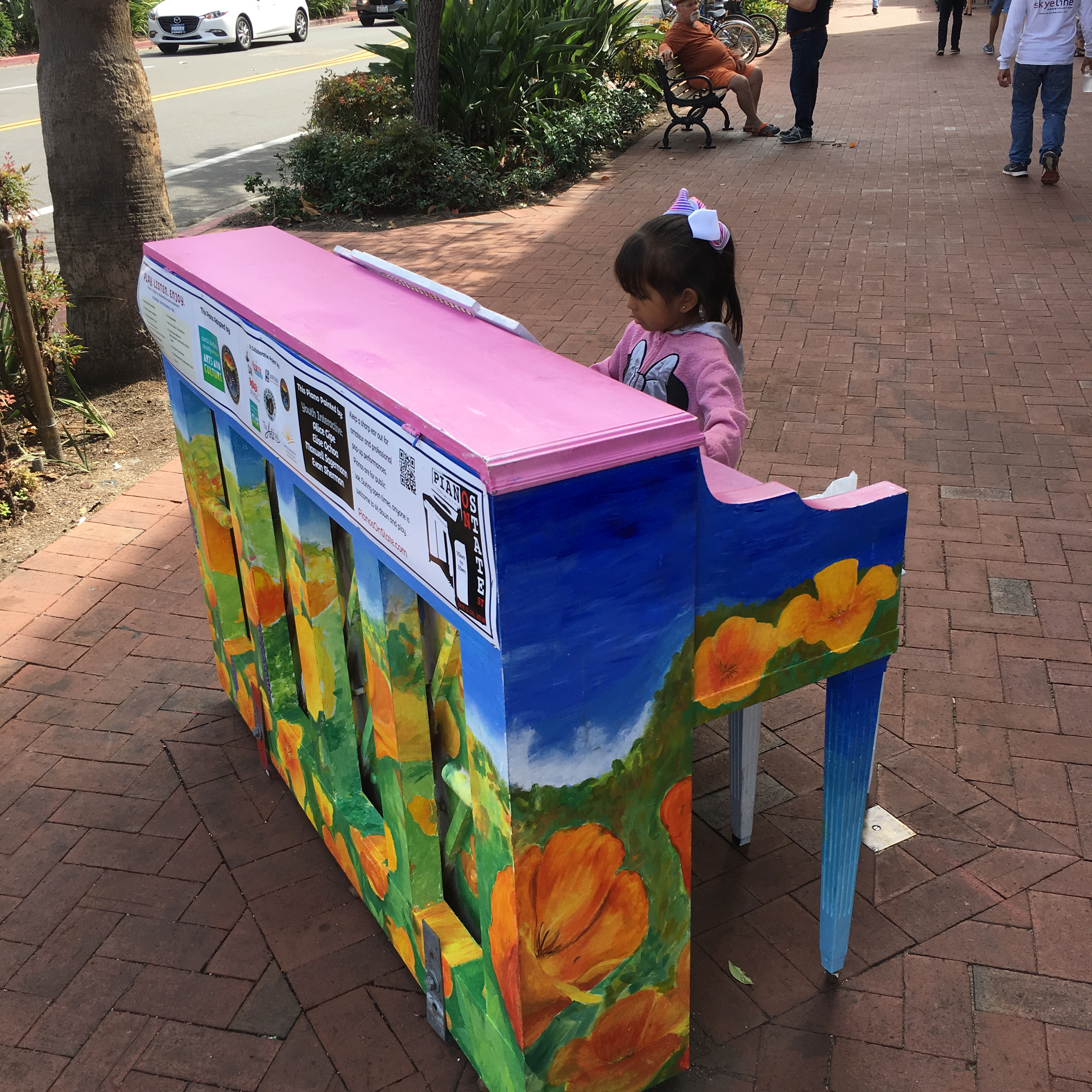 Little girl in a pink top playing a pink piano on State Street.
