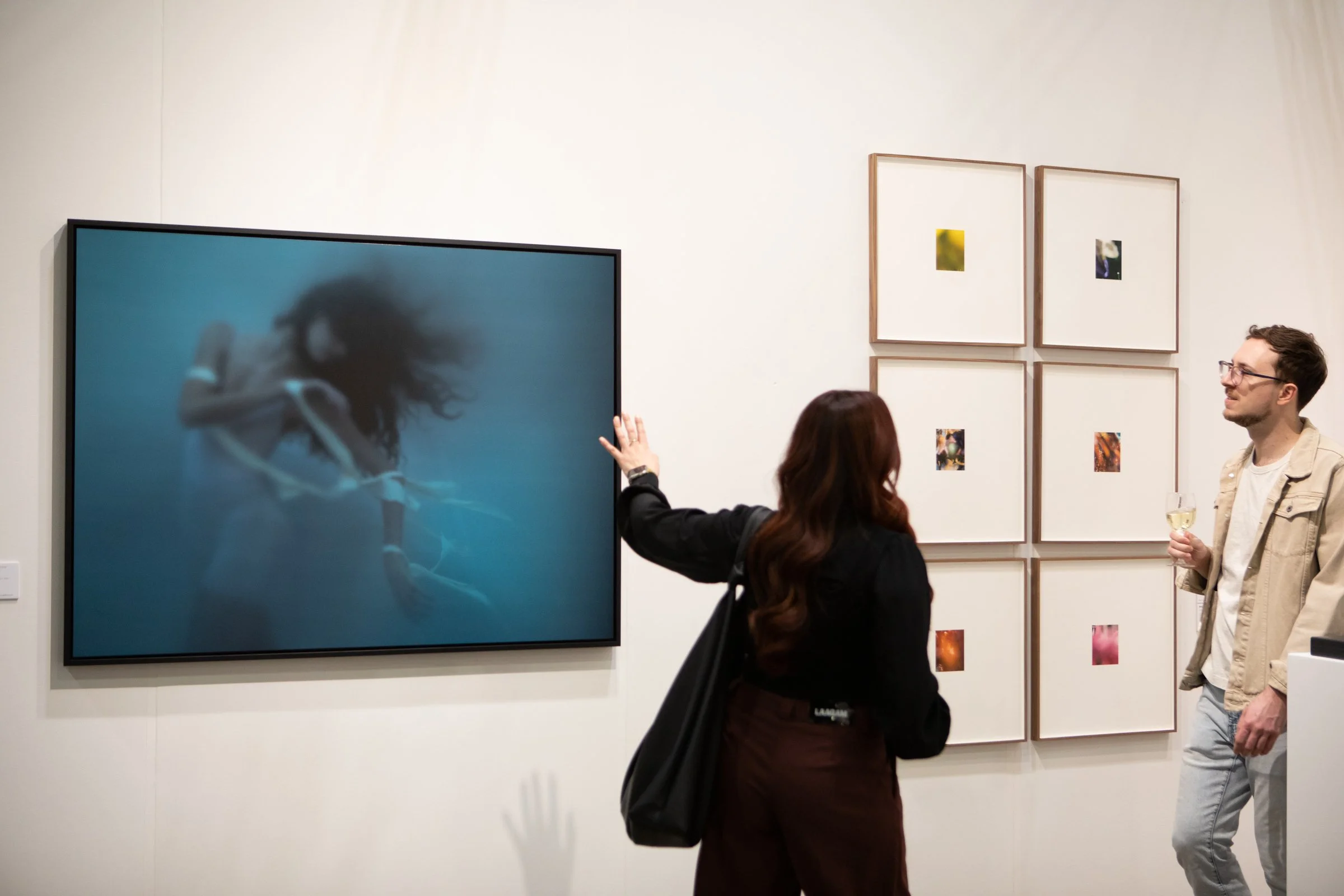 A woman in a black outfit standing in an art gallery with three landscape photographs of dogs on the walls behind her.