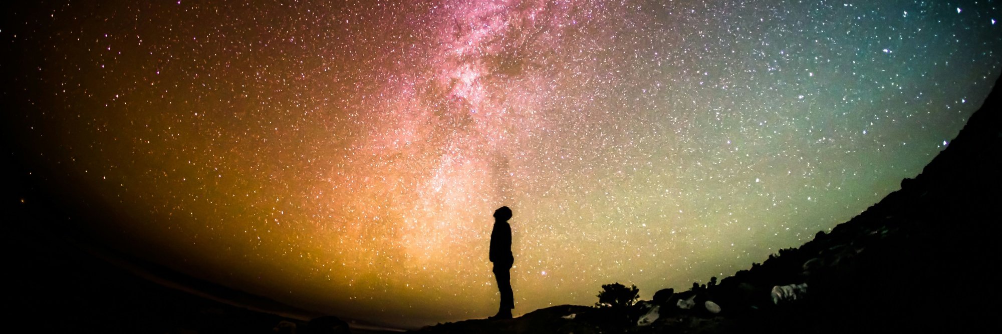 The silhouette of a person looks up to the night sky, and the spectacular colours of the milky way.