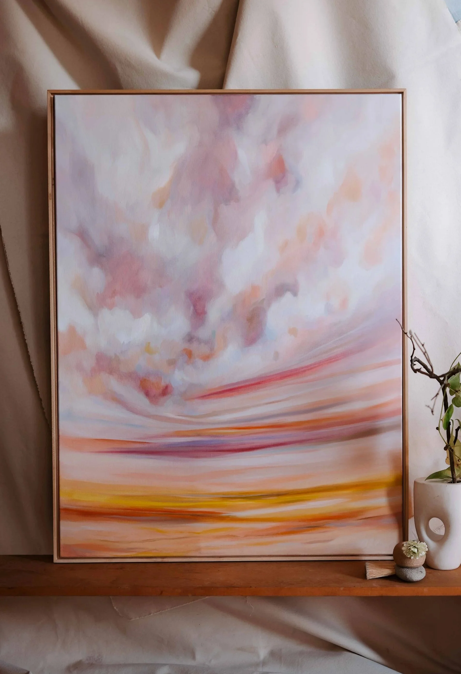 A close up of a thinly framed beautiful oil painting. The scene is of a sky at sunrise, pinky and orange and expansive and healing.