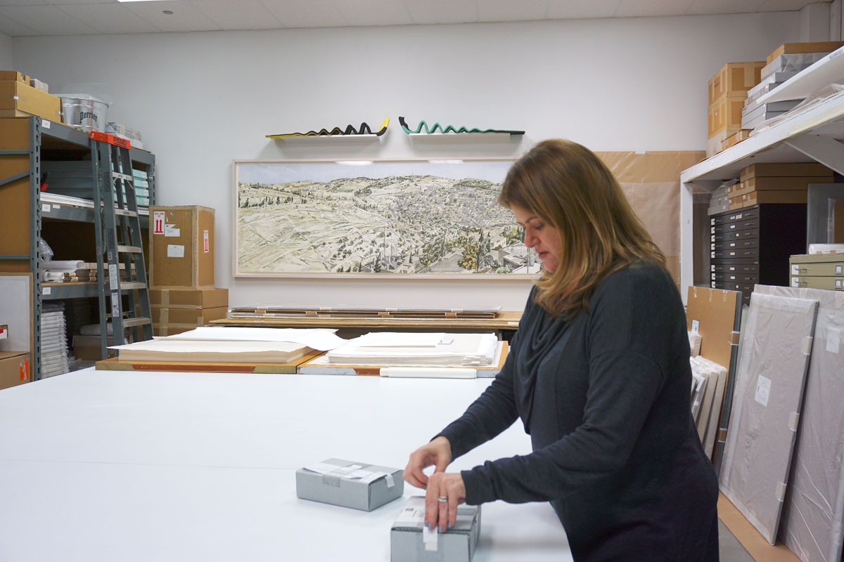 © 2019 Louise Levergneux. On wall in background: Philip Pearlstein, Jerusalem, Kidron Valley , 1989, heliorelief with roulette on wood, 40 x 119”. Kristin opening the boxes that contain Ed Ruscha’s artists’ books Me and The , and OH NO.