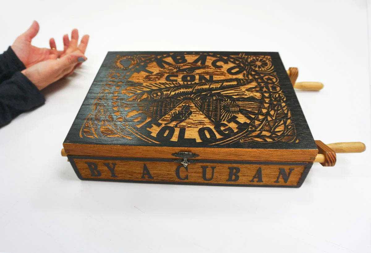 © 2019 Louise Levergneux. Abel Barroso, Tabaco con Ideologia (Cigars with Ideology), 2001, handmade Spanish cedar bas-relief “cigar box” with woodblock print (inside lid) and lithograph scroll-print (inside box) viewed by turning two hand-carved crank handles attached to moveable parts; TEXT by artist 9 x 16-3/8 x 3”.