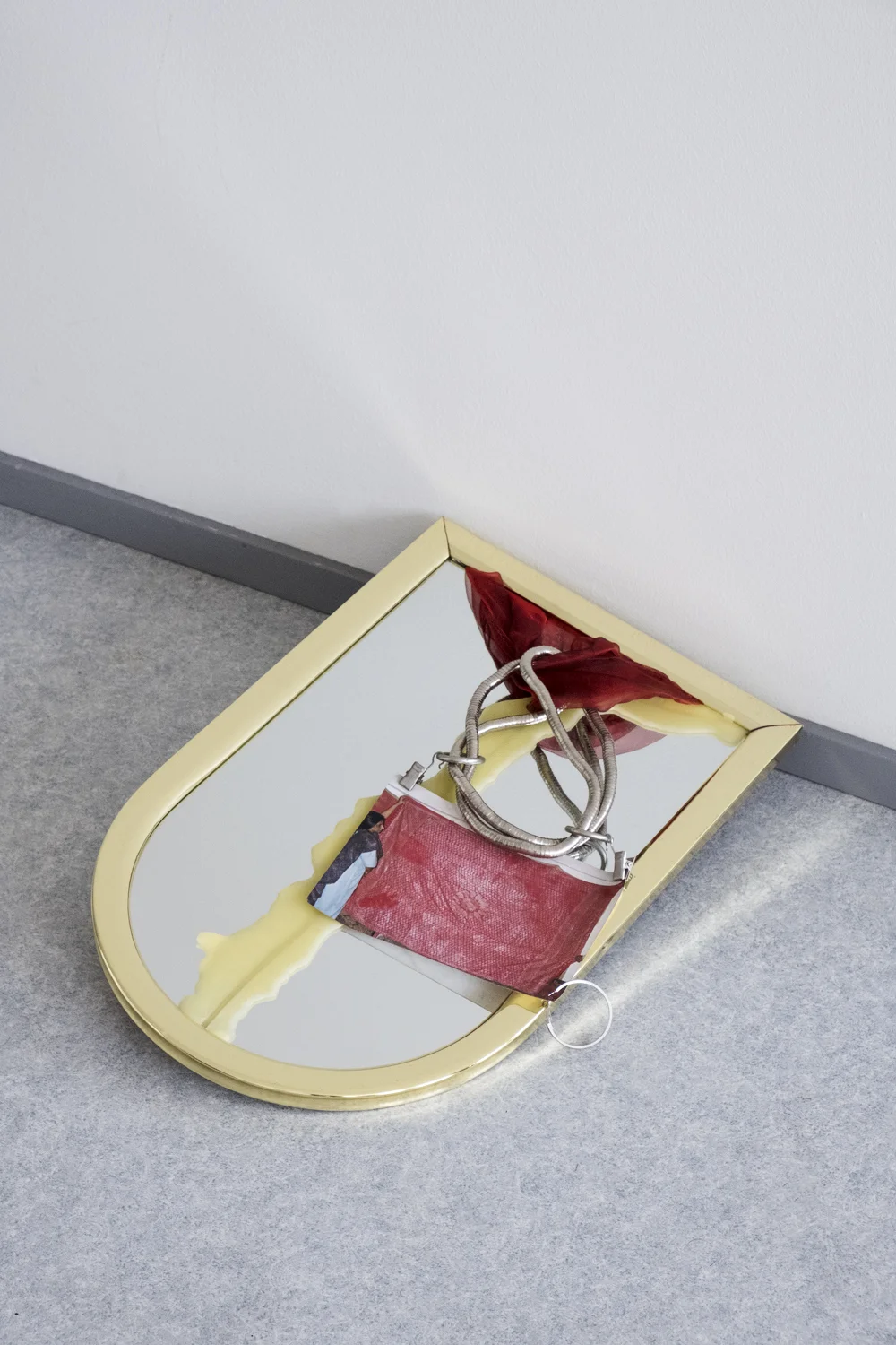 Vanessa Kowalski - Untitled (Foundation), 2018, Dimensions Vary According to Make-Up Routine Broken Mirror, Beeswax, Costume Jewelry Necklace, Curtain Clips (2), Found Photograph from New Delhi (Women Holding Silver Thread Embroidered Tapestry), Found Fabric, Hoop Earring Left by Summer Subletter, Door Stop. Photo by Vanessa Kowalski.