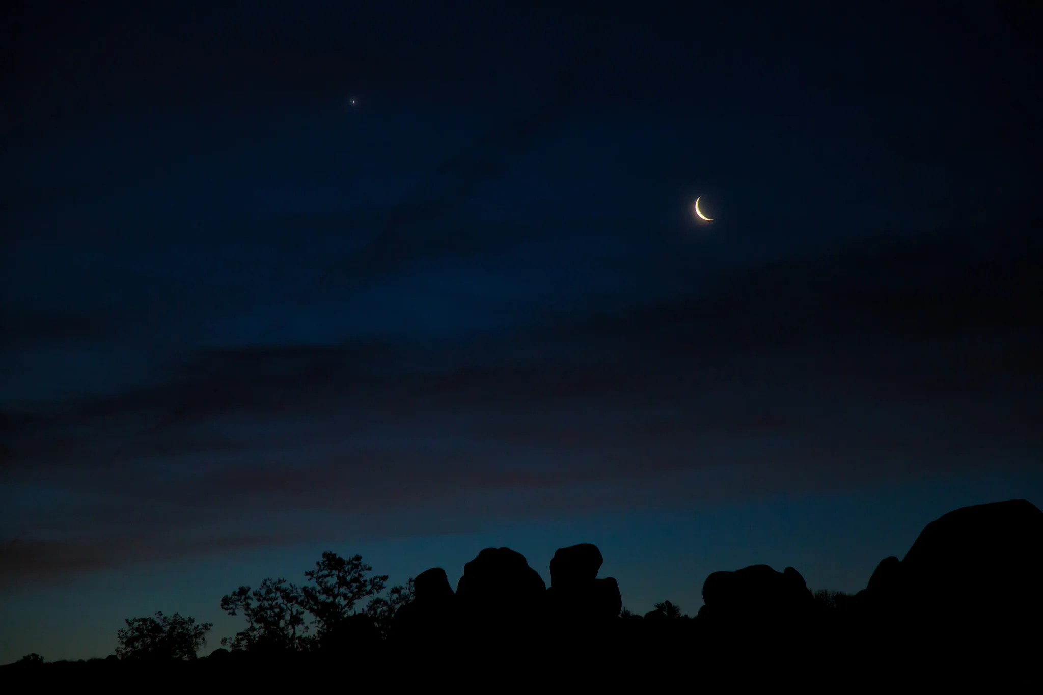 A waning crescent moon with planet Venus to the left just before sunrise at Skull Rock