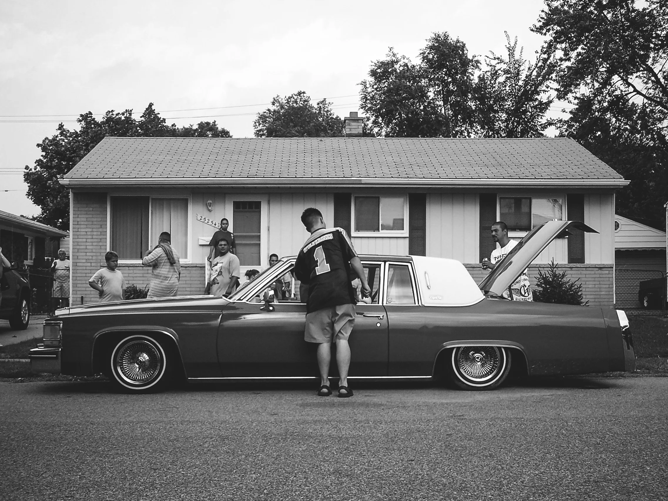 Chris of Por Vida Car Club goes to the door to hop his Cadillac on the street at Sergio’s BBQ. Warren, MI. (2005)