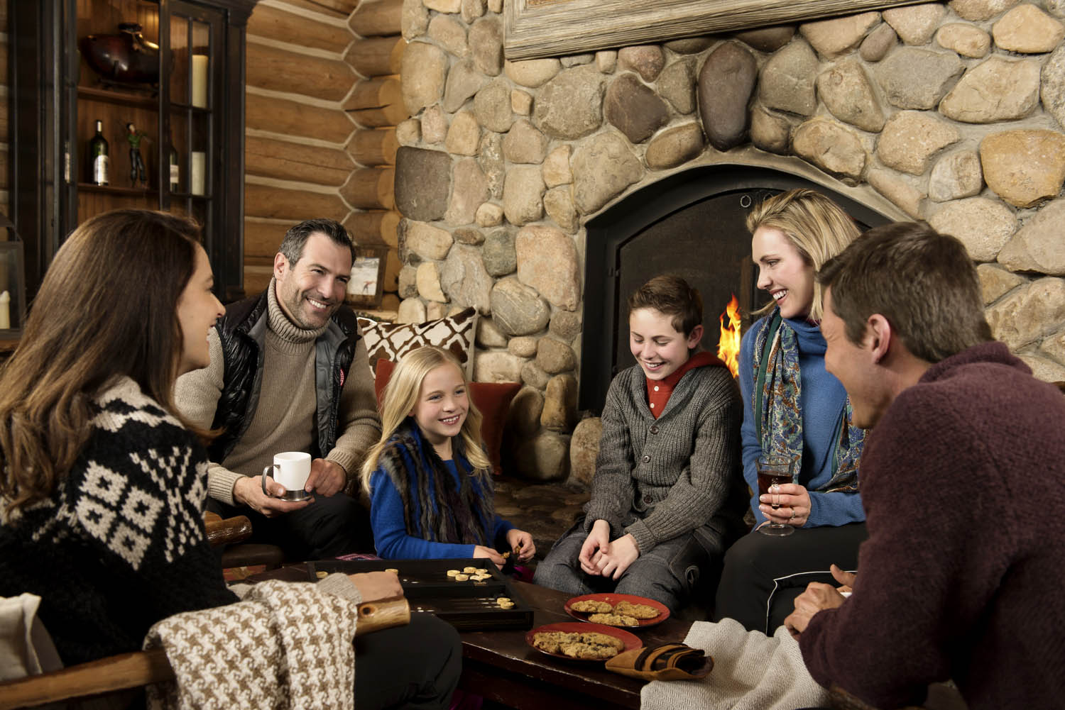 Family and group playing around fireplace at Beano's Cabin in Beaver Creek Colorado. Lifestyle advertising photography.