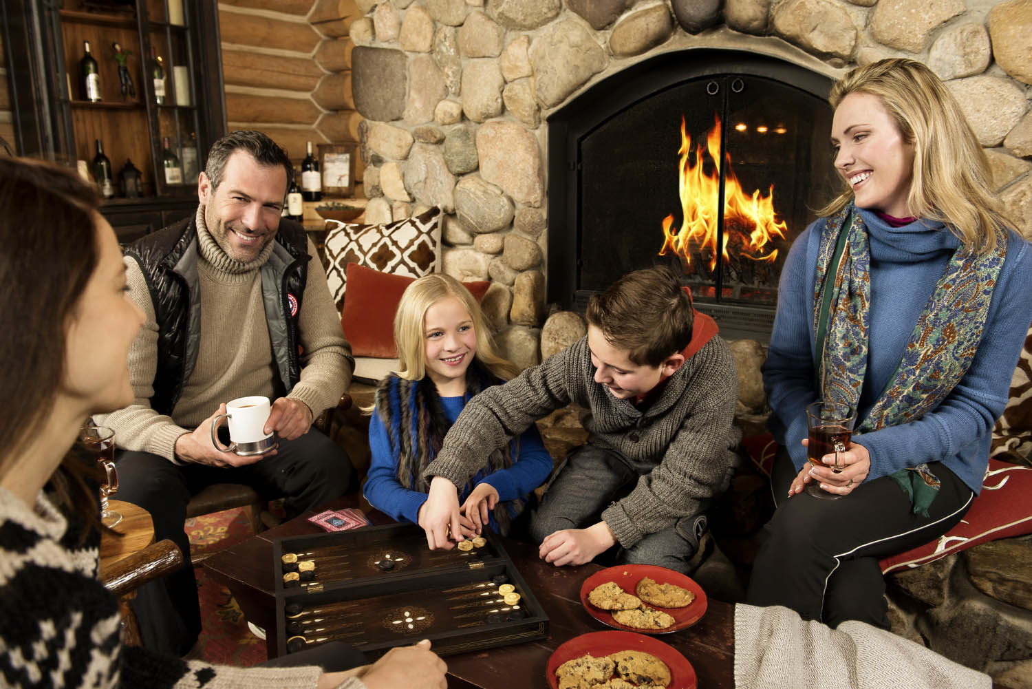 Family and group playing around fireplace at Beano's Cabin in Beaver Creek Colorado. Lifestyle advertising photography.