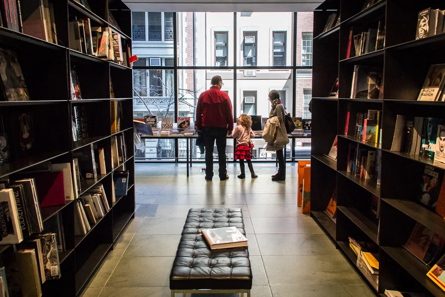 People browsing books inside a bookstore, with large windows and a city street outside.