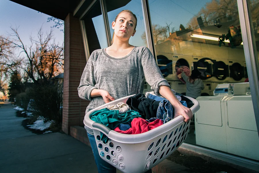 A woman with a laundry basket full of clothes outside a laundromat during autumn.