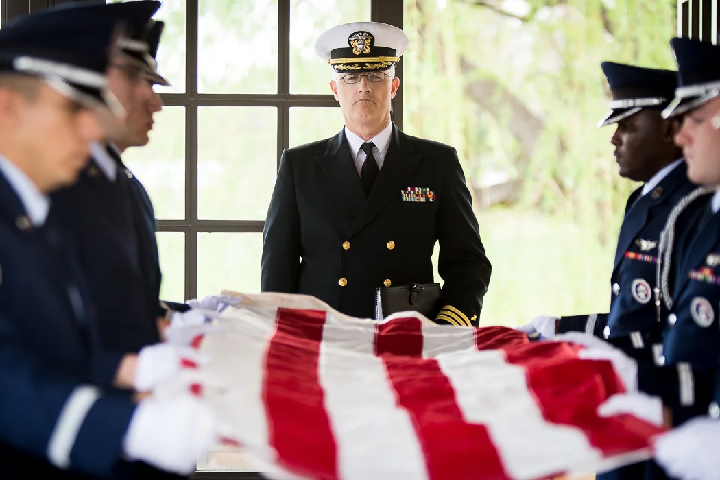 Military officers standing around a folded American flag during a flag-draped casket ceremony.