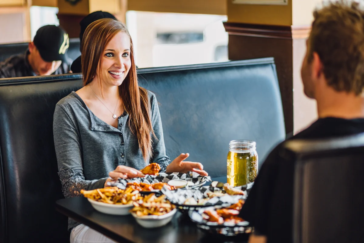 A woman and a man sitting at a restaurant table, enjoying food and a glass of beer, engaging in conversation.