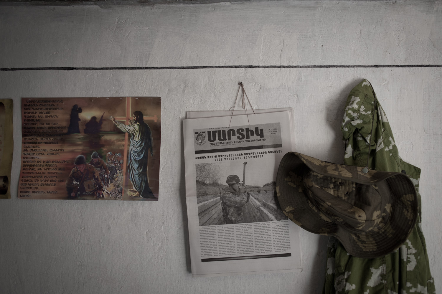  On the walls of a dugout on the Mataghis frontline hangs a religious poster discouraging violence among the military ranks, a soldier's hat and jacket, and a copy of the official military newspaper.  