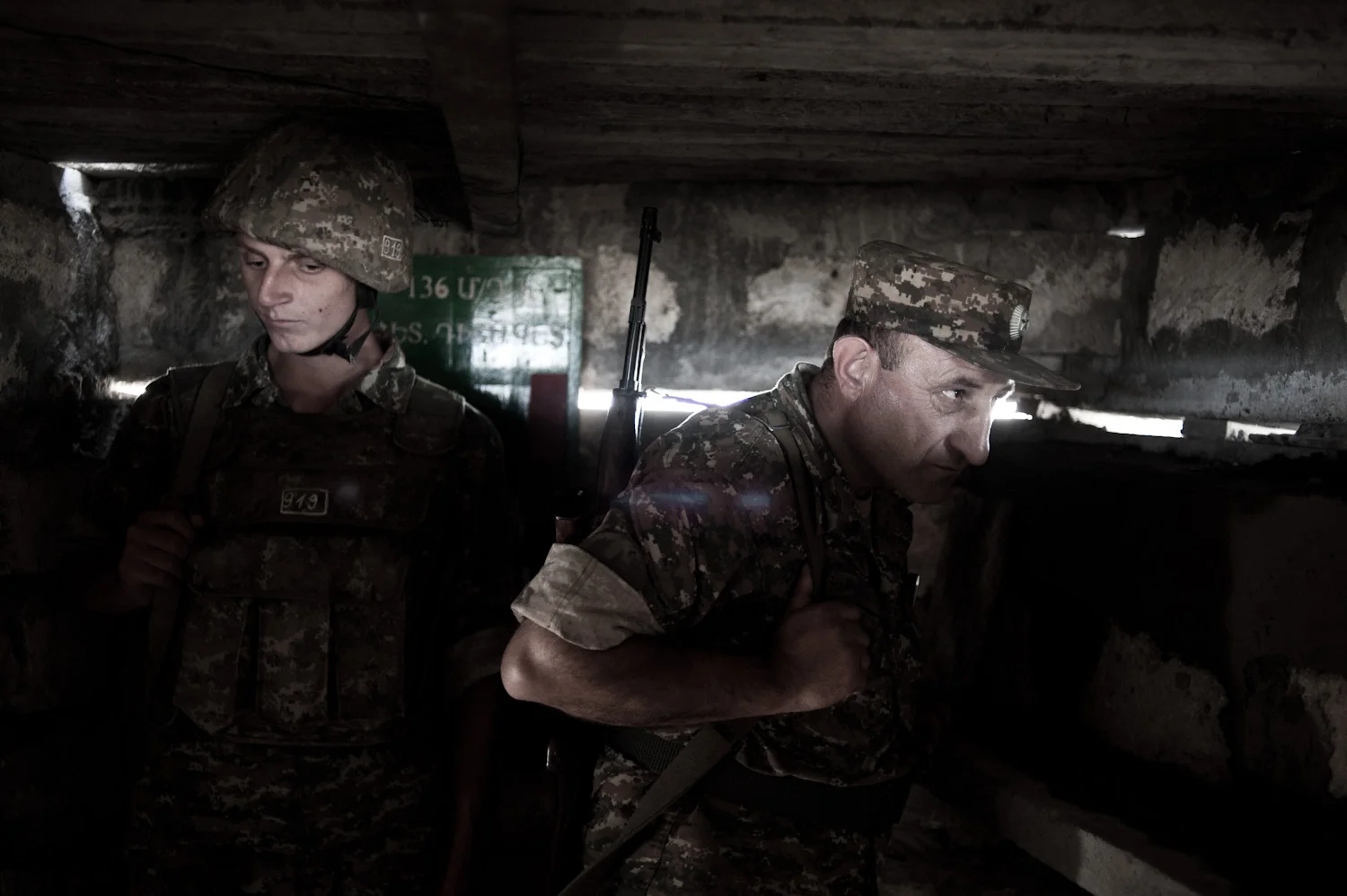 Colonel Alik Sargsyan watches the Azerbaijani frontline located 30 meters from his position at a lookout post, with young conscript Arman in the background.