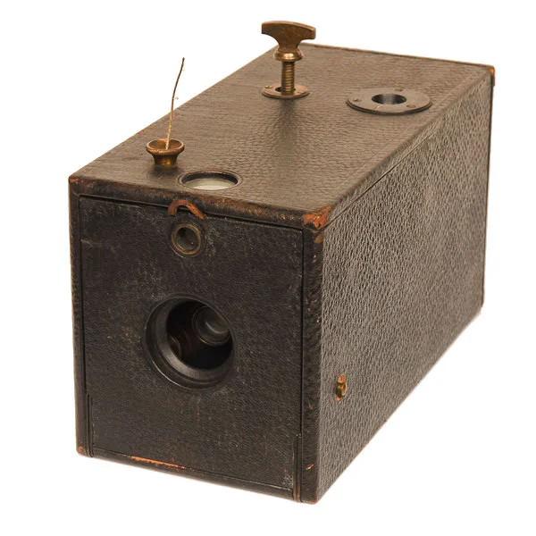 Kodak Box Model 1 1889-1895. Out of such a simple box camera came a giant. The Kodak Model 1 Box camera was the model George Eastman marketed to the public so successfully. It was also his first production model. The camera sold for $25 with 100 exposures of film preloaded and the amateur only needed to point and pull the wire (pre-shutter button). The winding key at the top enabled selfwinding. But the genious lay in the marketing. These cameras could be sent back to Eastman to have the film processed and printed, A camera reload only cost $10. So a happy customer could be a customer for life. This was the begining of a very successful photographic products business known as Eastman Kodak.
