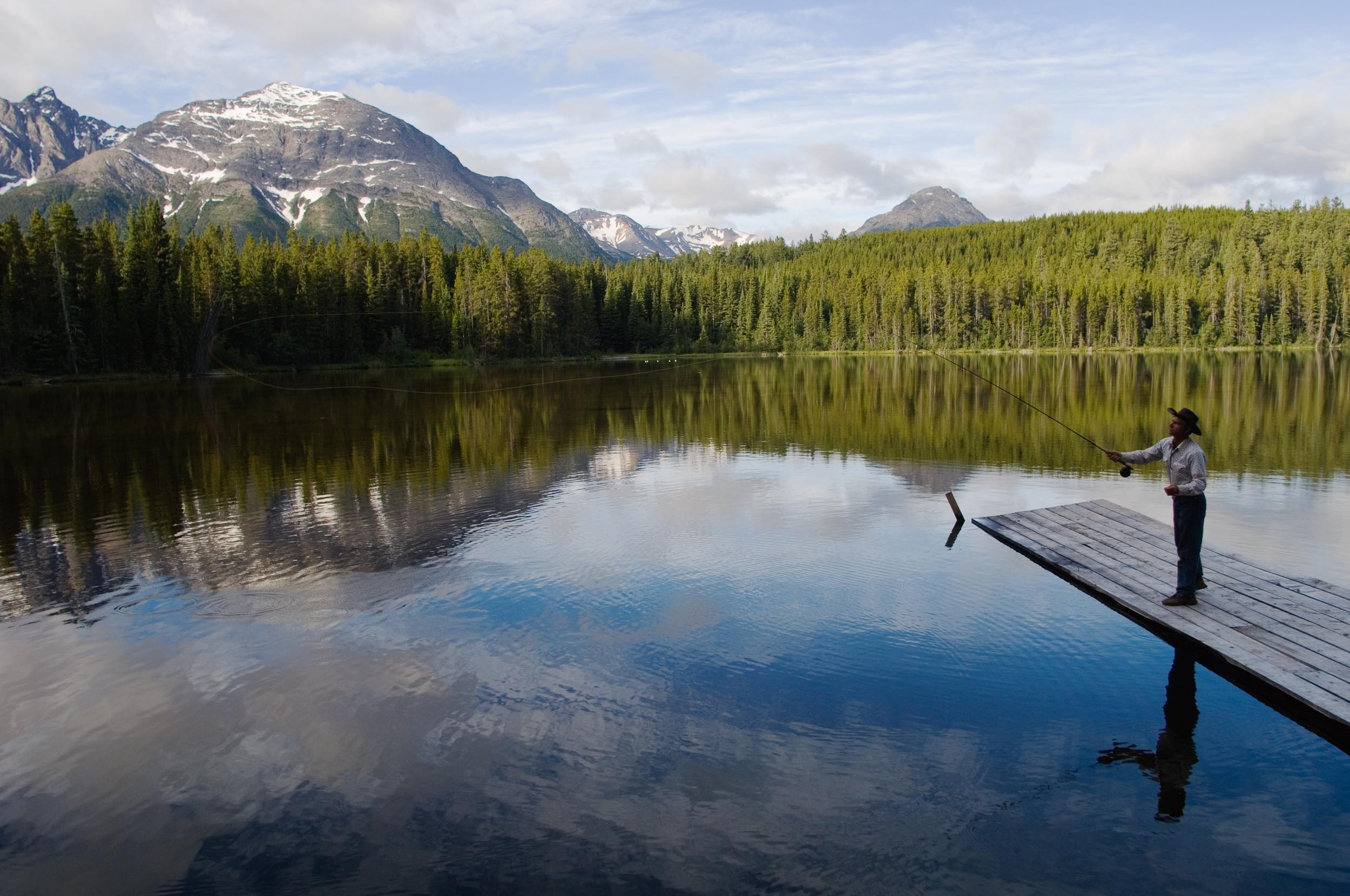 Fishing from a dock with views of the mountains at Cheshi Lake. Credit: Destination BC/Albert Normandin