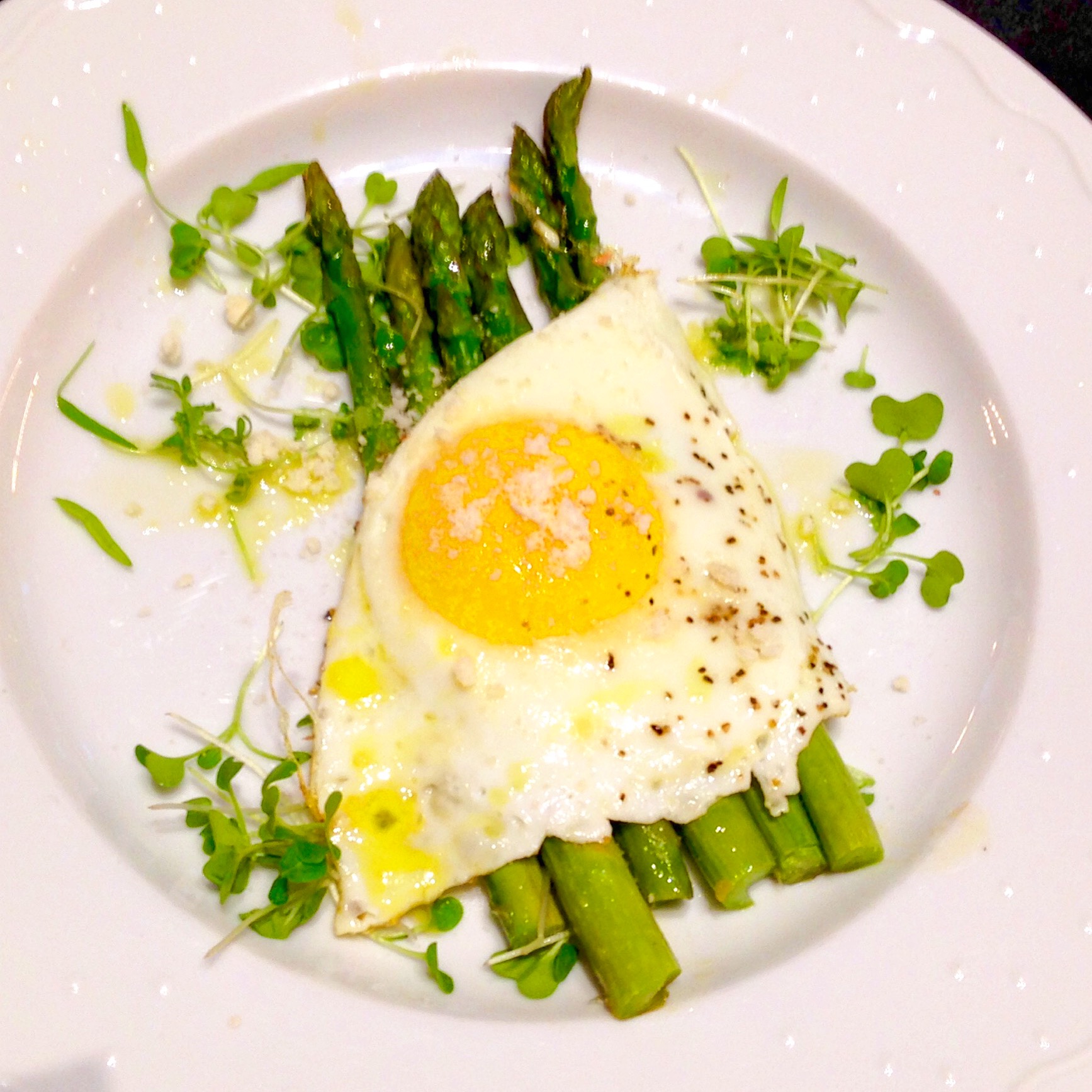Olive oil-cooked egg on asparagus spears with microgreens, parmigiano, and truffle butter