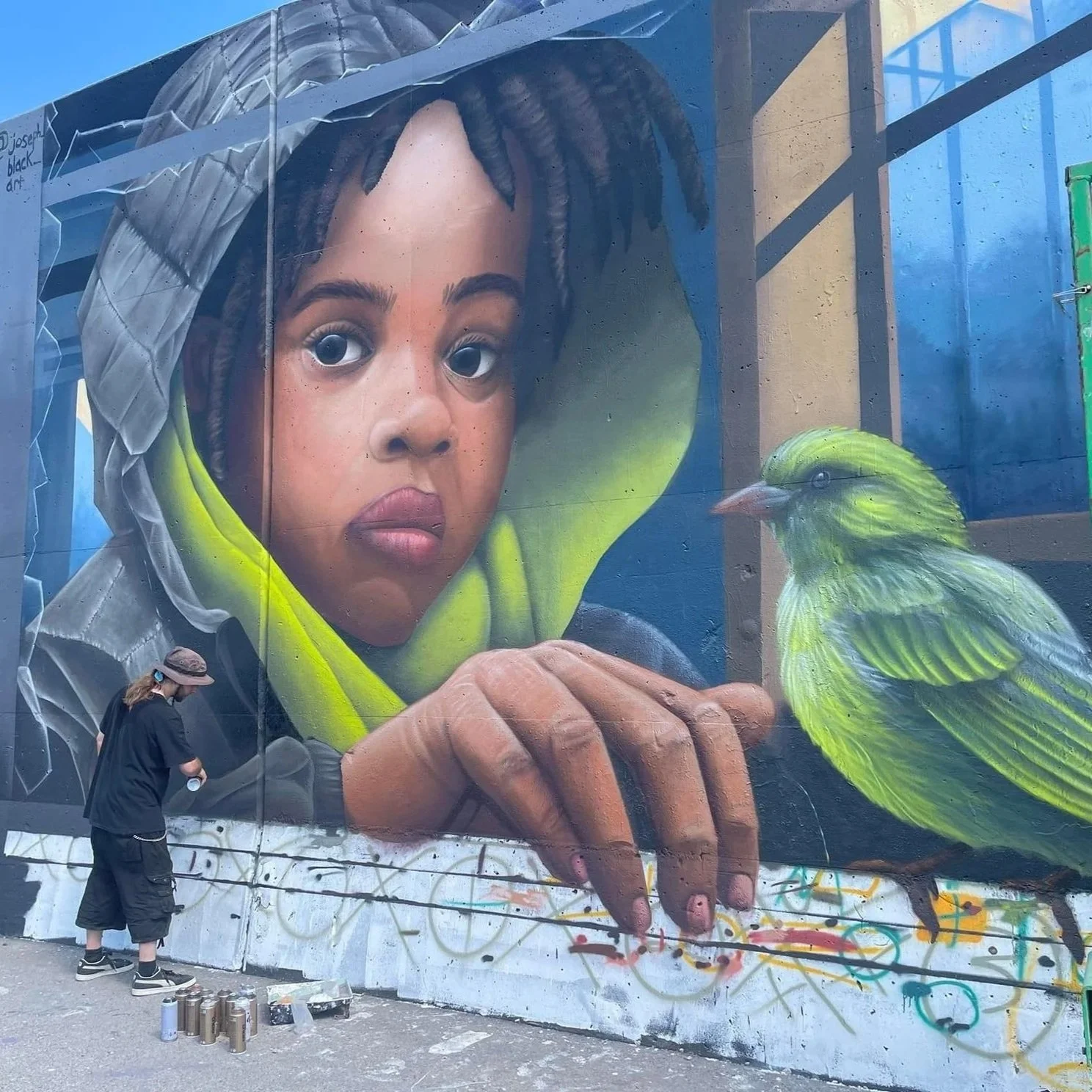 A Little Bird Told Me mural by Joseph Mueller, depicting a young boy in a hooded jacket peering out a window with a green bird on its sill