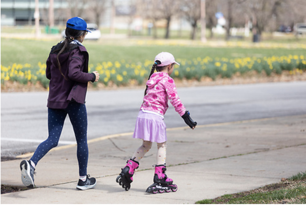  A caregiver jogs along a roller skating child. 