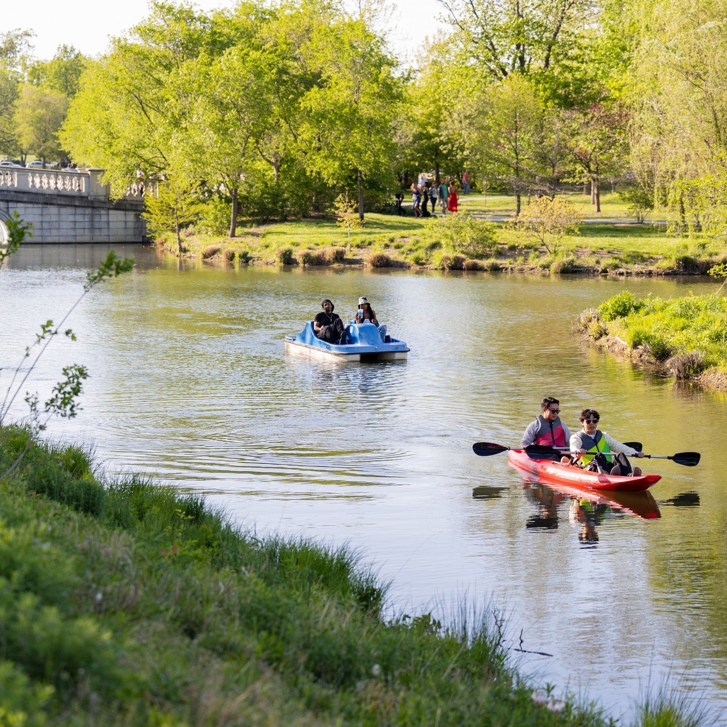 POV you visit @PaddleForestPark and it's decision time:
💙 team paddle boat
❤️ team kayak

{Image: Two people in a blue paddle boat and two in a red kayak are moving along a waterway that is lined with green grass. A stone bridge and a cluster of peo