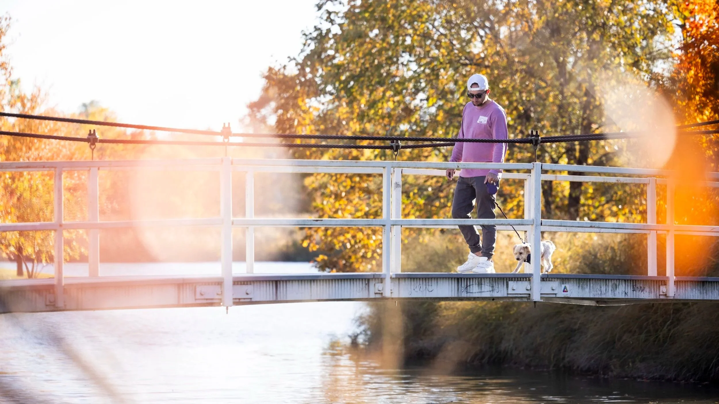 A visitor leads their leashed dog across the Suspension Bridge in autumn.