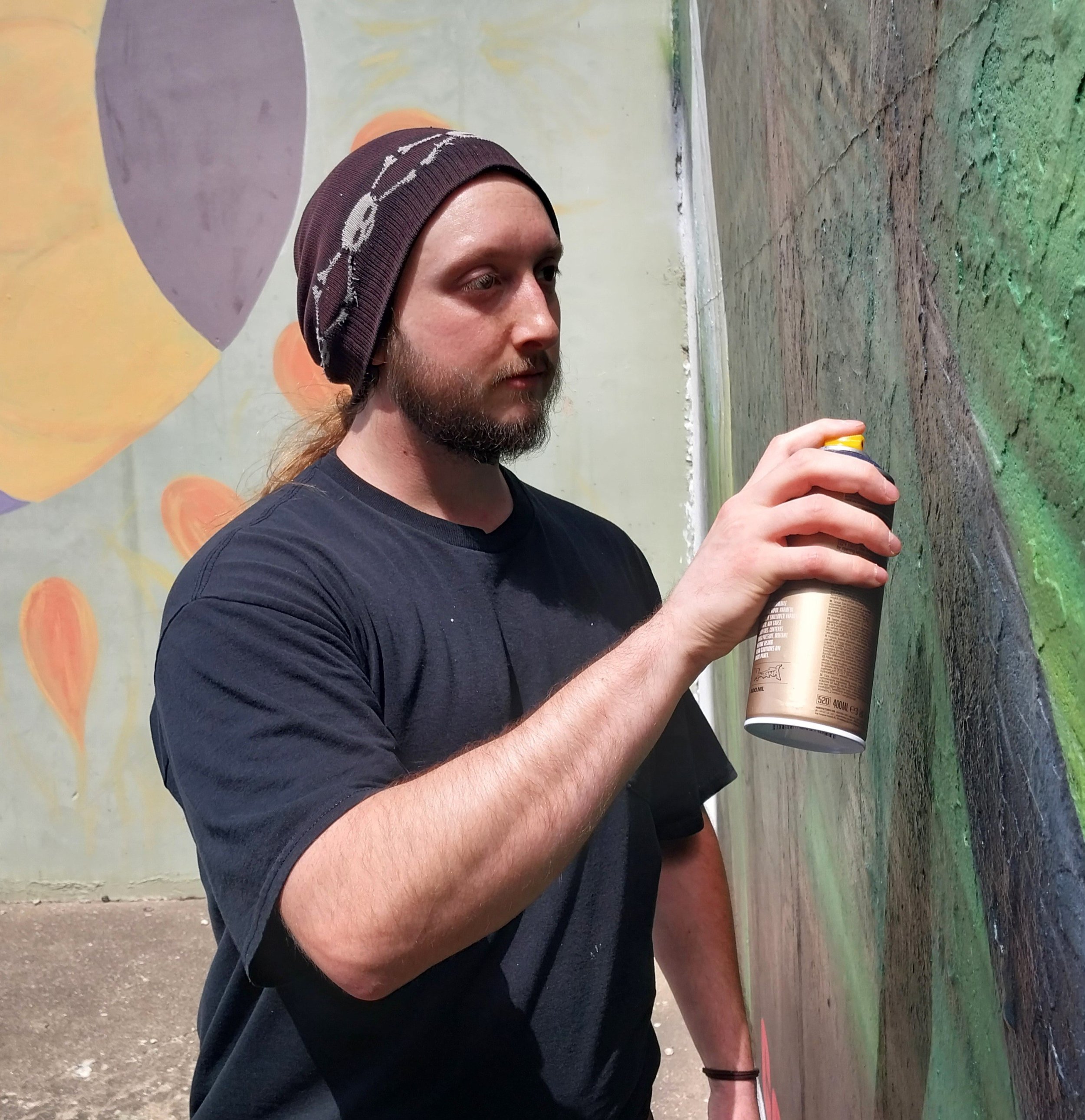 Joseph Mueller, a local artist, using a can of spray paint to complete a mural