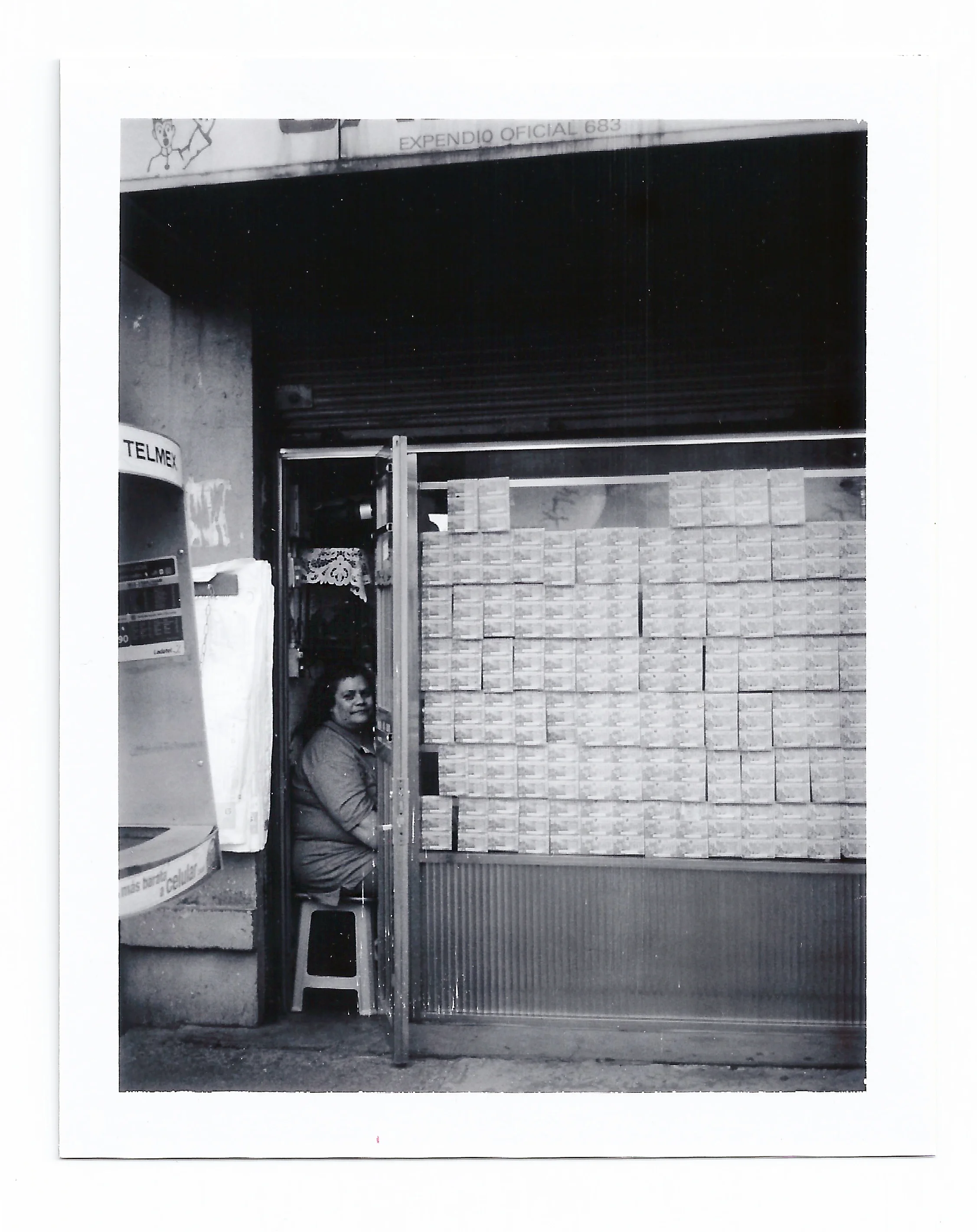 Down the street, I see a little shop with the windows covered with some sort of tapestry made out of Lottery tickets. Inside the shop, a woman curls her eyelashes. I ask her if I can take a picture. She immediately agrees and looks my way, sitting peacefully on a red Coca-Cola plastic stool. I take her picture in that little nest that she has made for herself inside the shop. I go back to Julien and he is still figuring out the LED sign situation. I sit again on the stool and wait for the Polaroid to be ready. “Qué bonita, no?” Julien says as I separate the image from its negative. We leave the electric shop and walk down the street. I show the Polaroid to the Lottery woman, who is now tweezing her mustache. She thanks me for taking her picture.