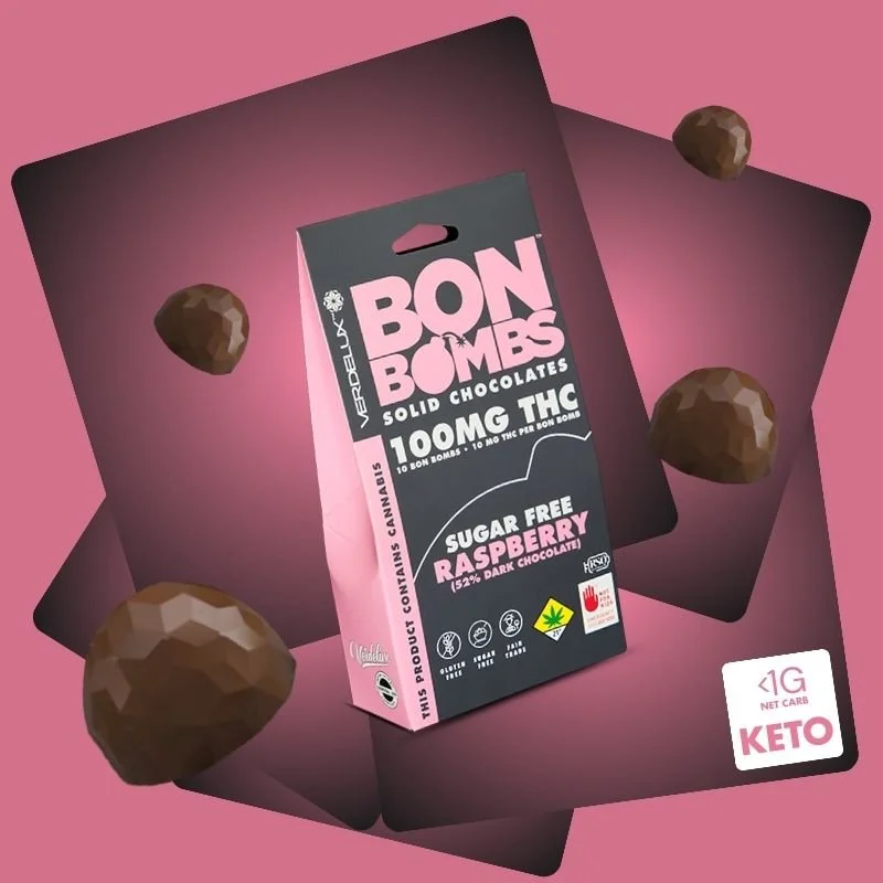 A pink background featuring a package of Bon Bombs solid chocolates, with raspberries flavor, surrounded by five small chocolate candies, and a white label indicating they are sugar-free, raspberry flavored, keto-friendly, with 100mg THC.