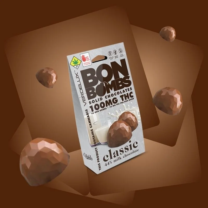 A cardboard box opening to reveal a chocolate product called Bon Bombs, labeled as solid chocolates with 100mg THC. The box features a picture of chocolate bon bombs and a glass of milk, with the text 'Classic' and '44% milk chocolate'.