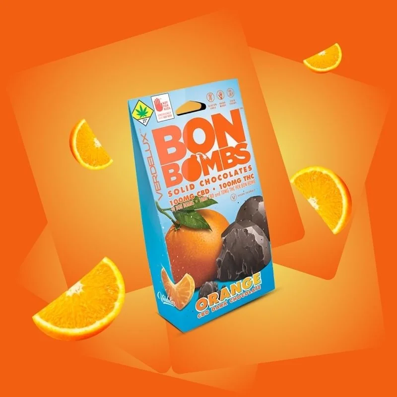 A box of Bon Bombs solid chocolates with orange flavor, containing 100mg of CBD and THC edibles, surrounded by orange slices on an orange background.