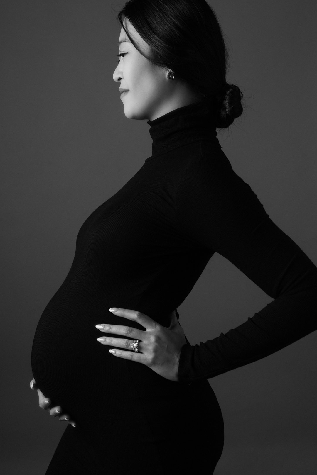 Black and white profile of pregnant woman in black turtleneck, hands on belly.