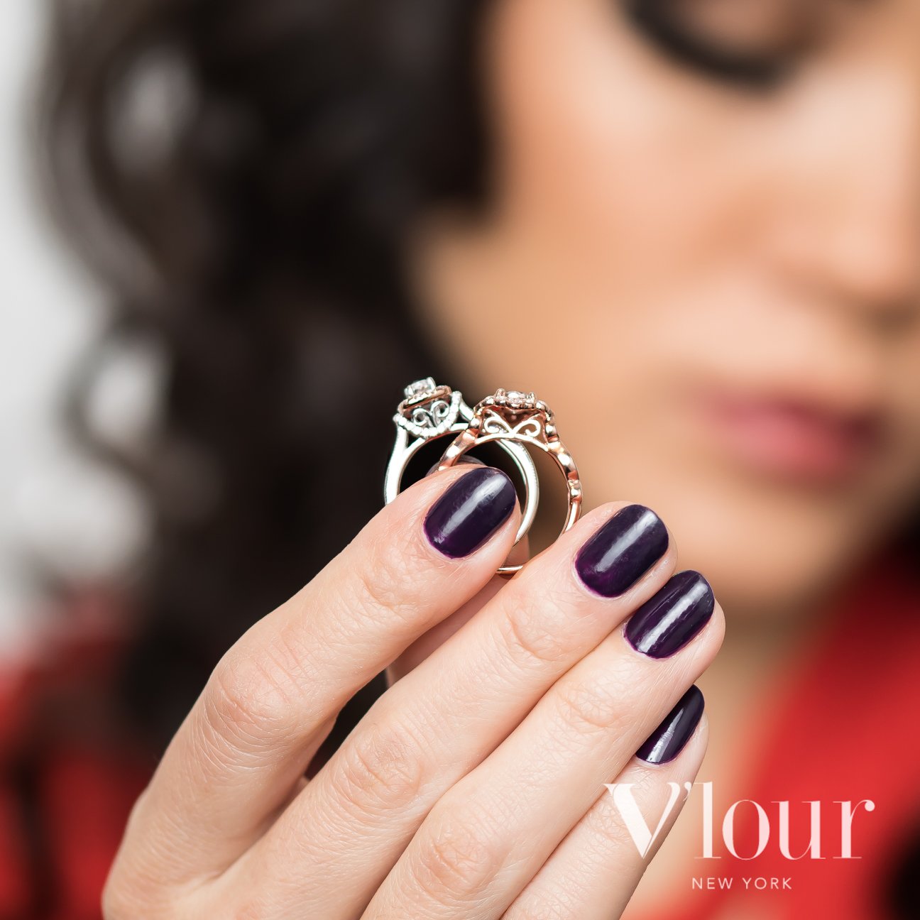 Close-up of a woman holding two diamond rings with intricate designs, featuring purple nail polish and a blurred background.