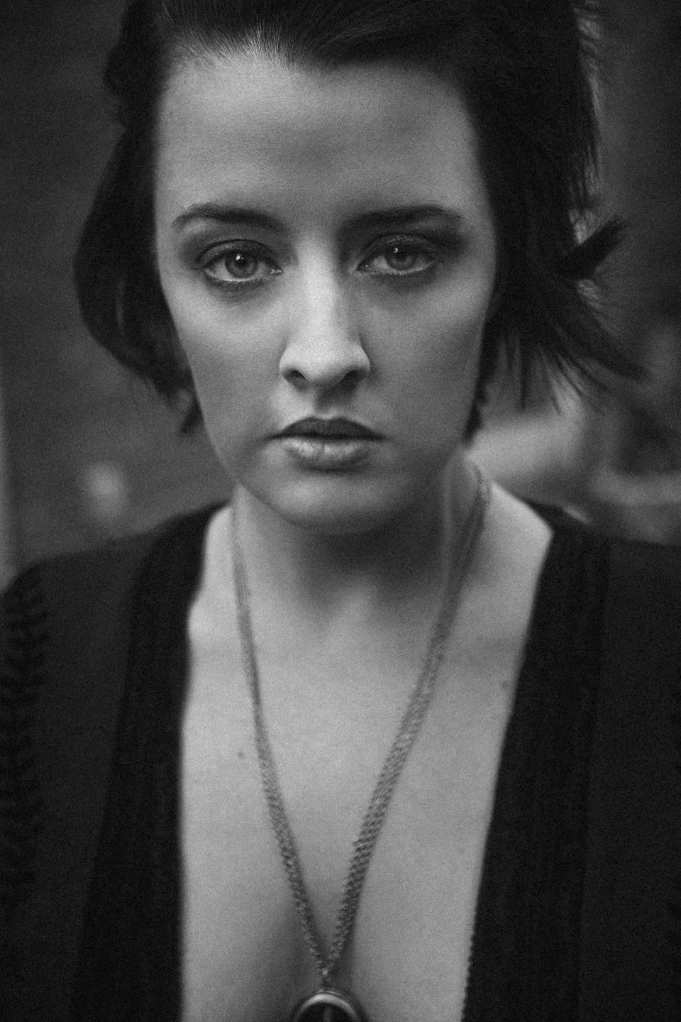 Black and white portrait of a woman with short, dark hair, intense gaze, wearing a necklace and dark clothing.
