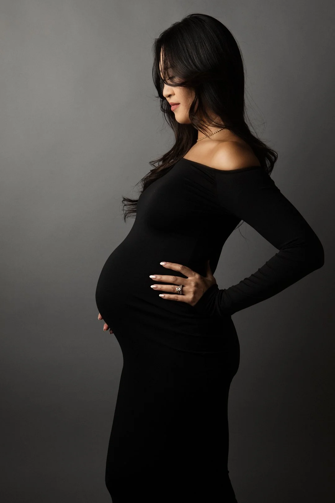 Side profile of a woman in a black dress holding her pregnant belly.