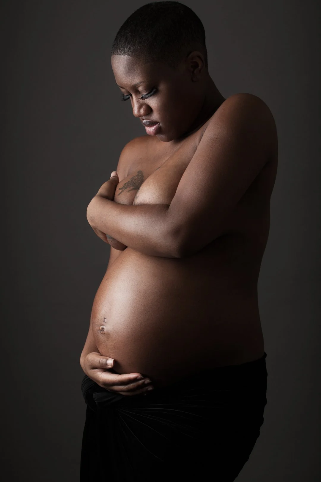 Pregnant person embracing belly with one hand and covering chest with the other.