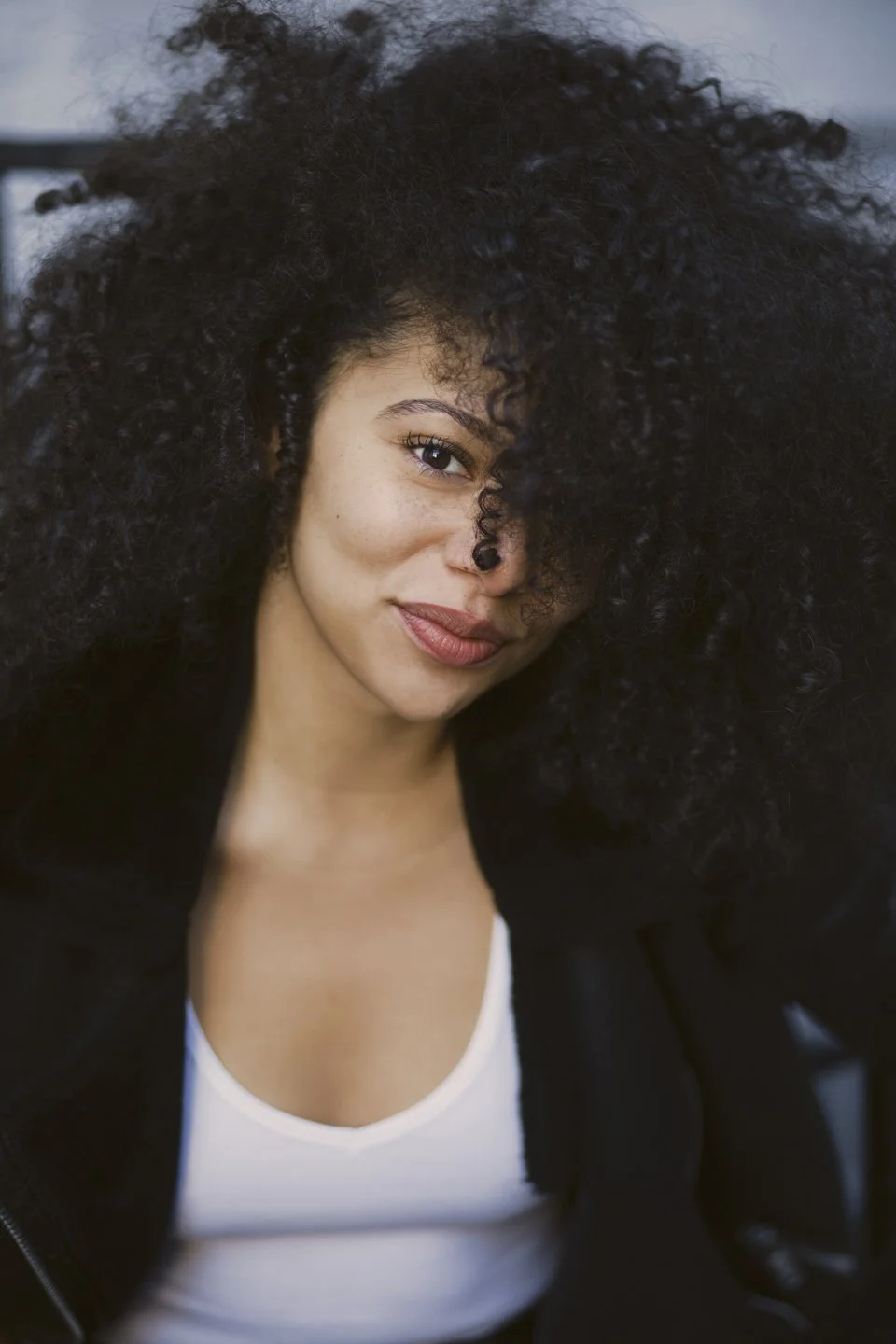 Close-up of a woman with curly hair, smiling slightly, wearing a black jacket and white top.