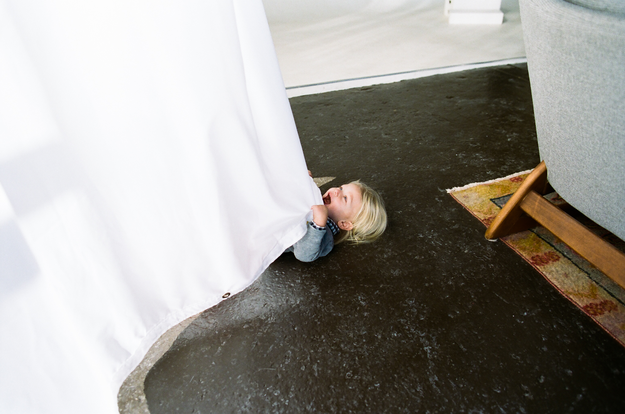 Young boy hiding in a curtain.