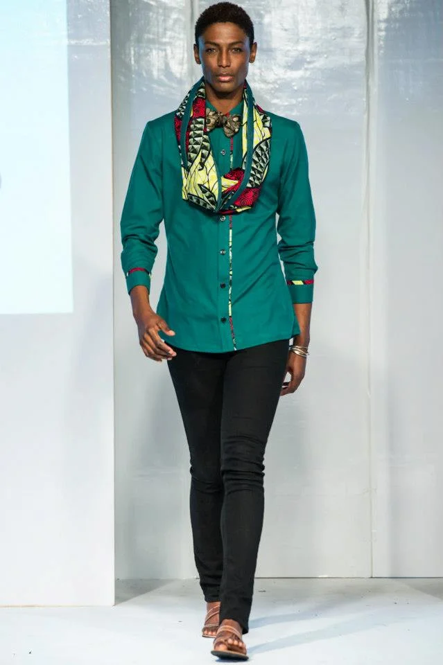 A woman walking on a runway wearing a teal button-up shirt, black pants, tan sandals, and a patterned scarf around her neck.