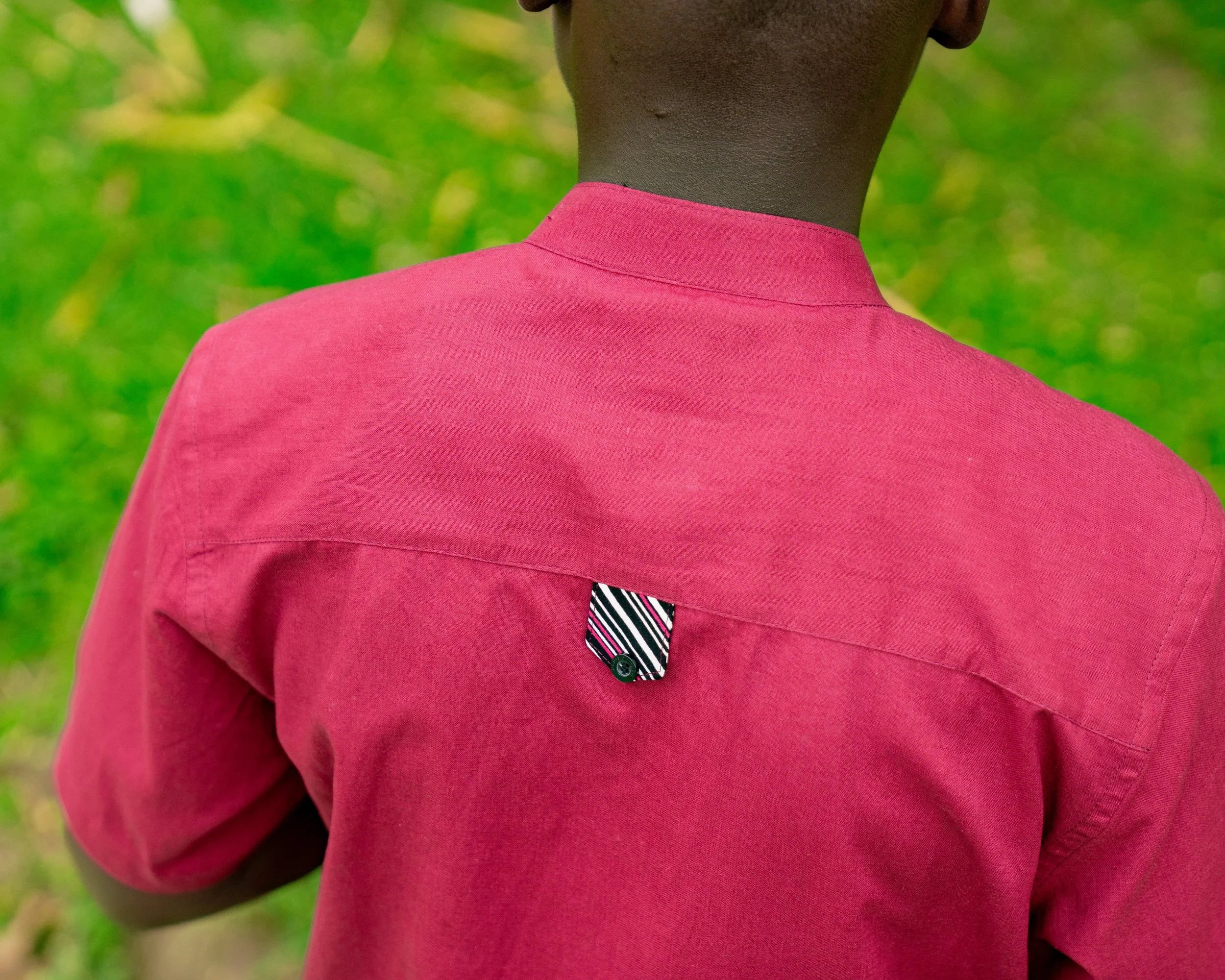Close-up of a person's shoulder and neck, wearing a pink shirt with a tie, against a blurred green background.
