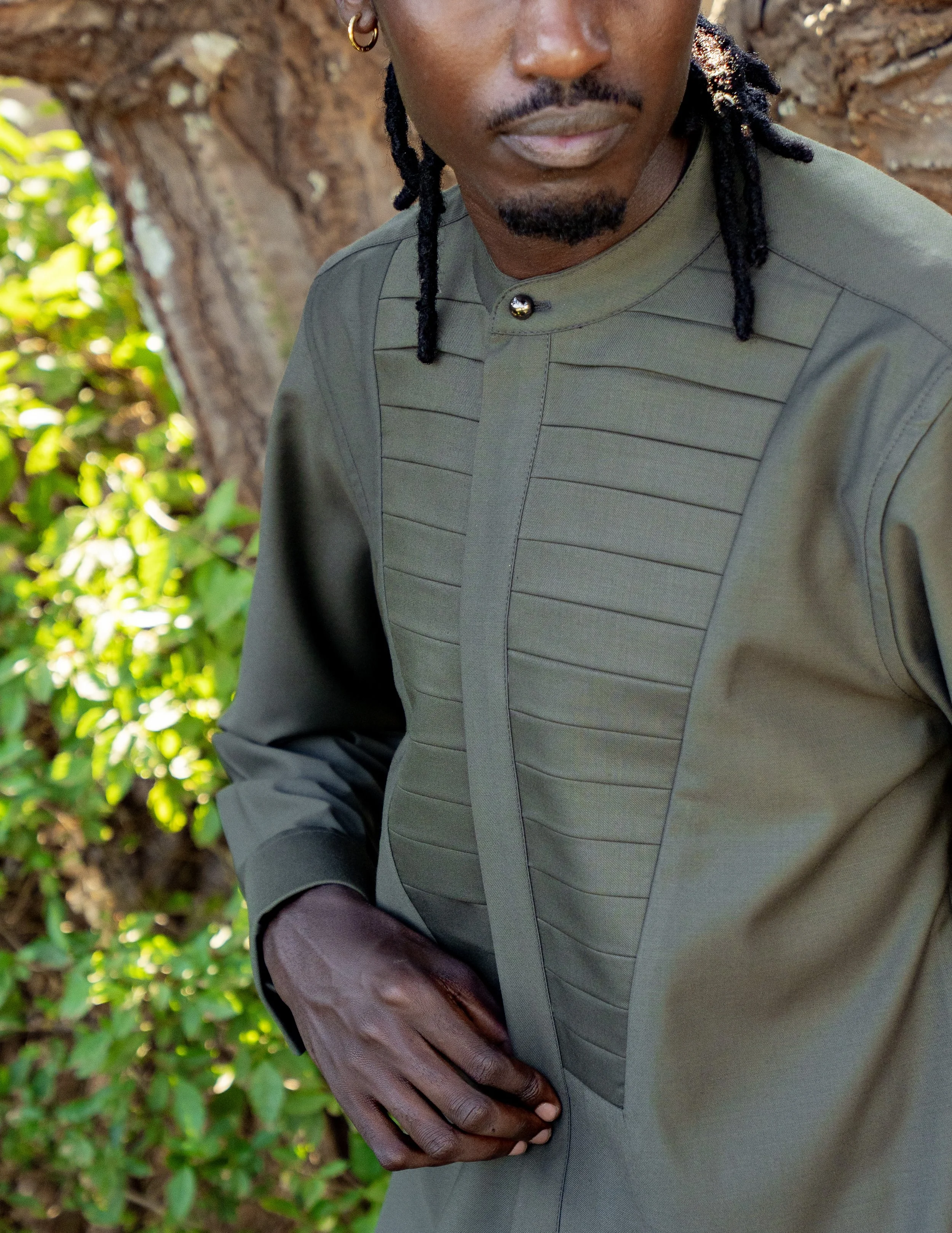 Person wearing a green shirt with pleats on the chest, standing outdoors with tree in the background
