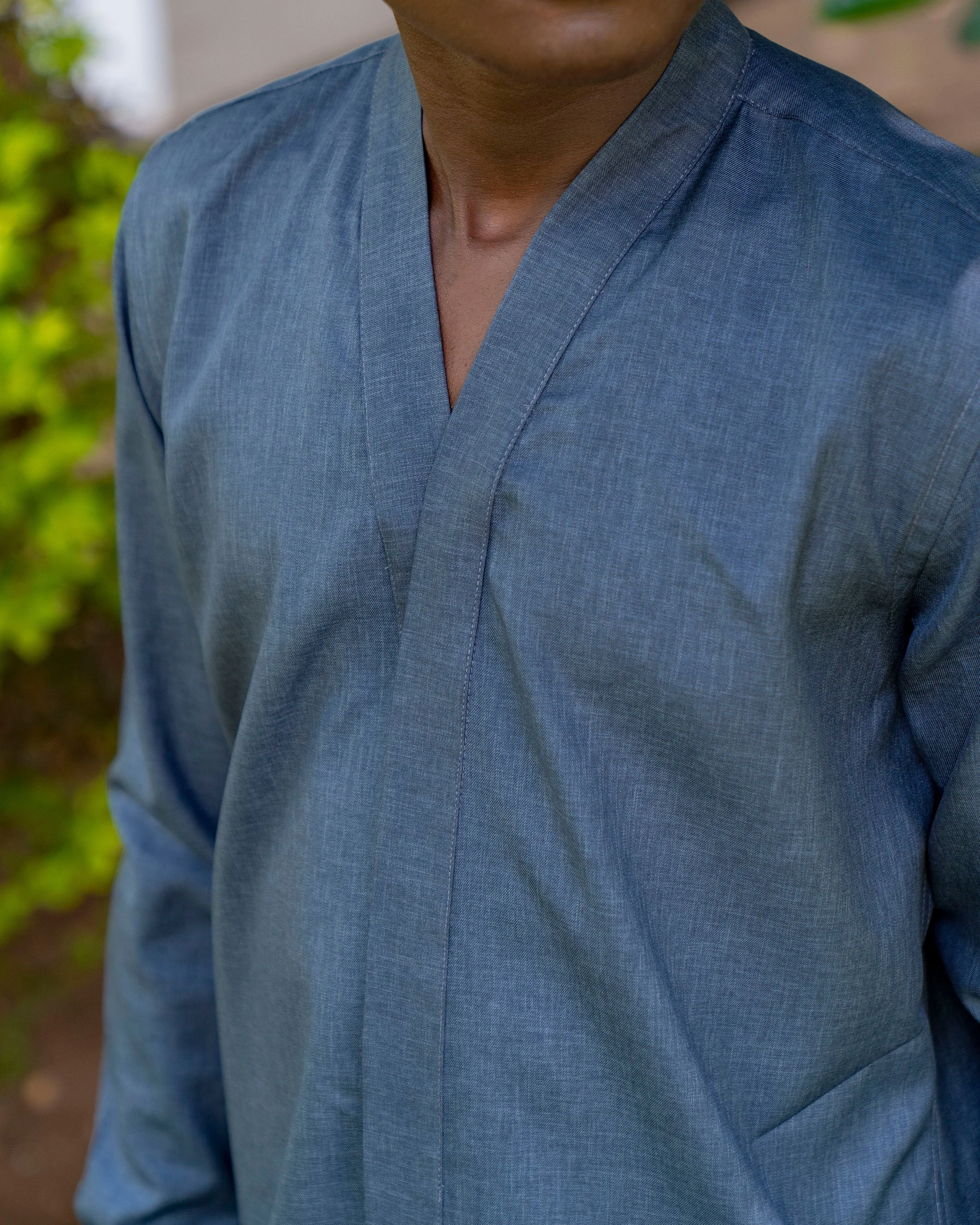 Close-up of a person wearing a blue traditional v-neck shirt, with a focus on the chest and neck area, against a blurred outdoor background.