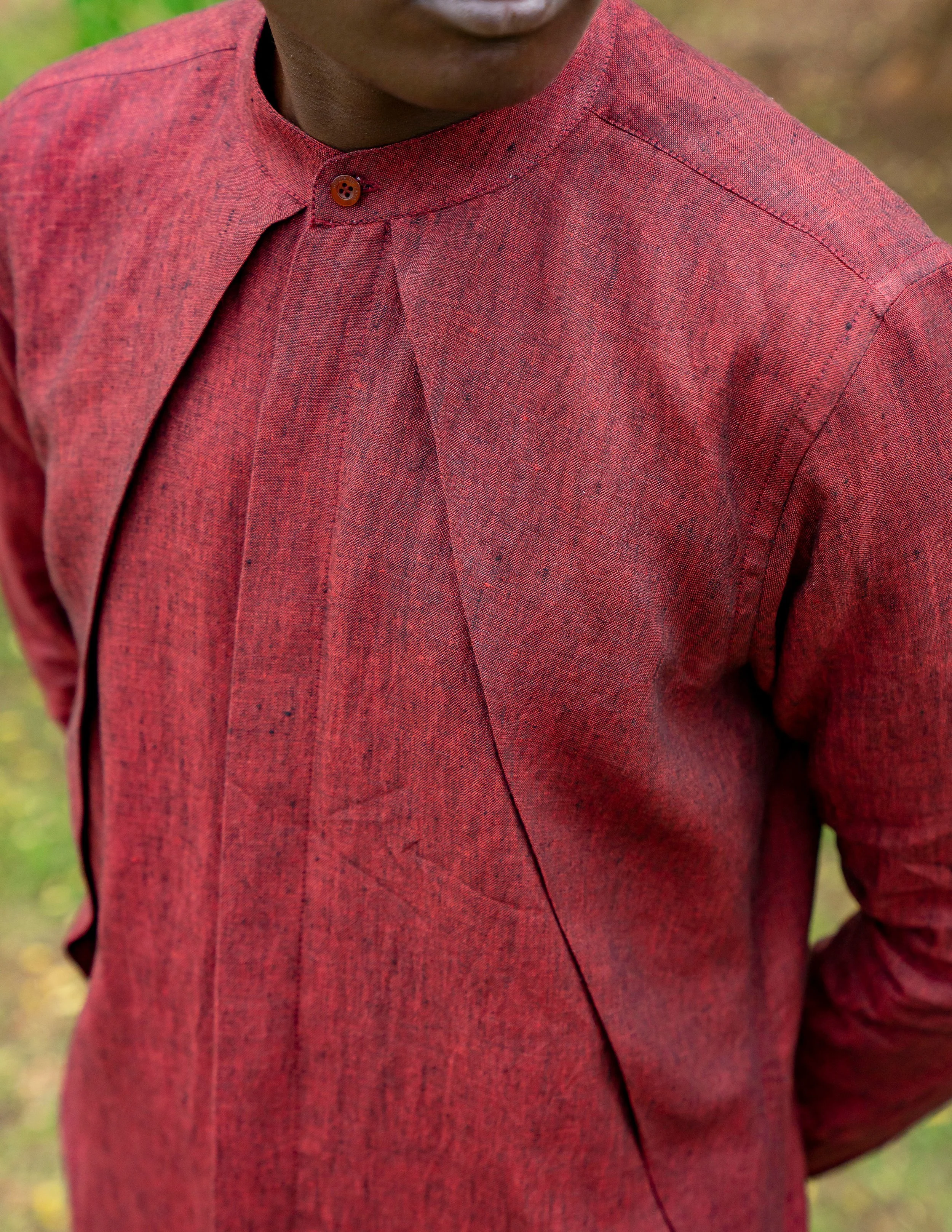 A person wearing a red shirt with a stand-up collar and a single brown button at the neck. The shirt has a textured, speckled pattern and visible seams.