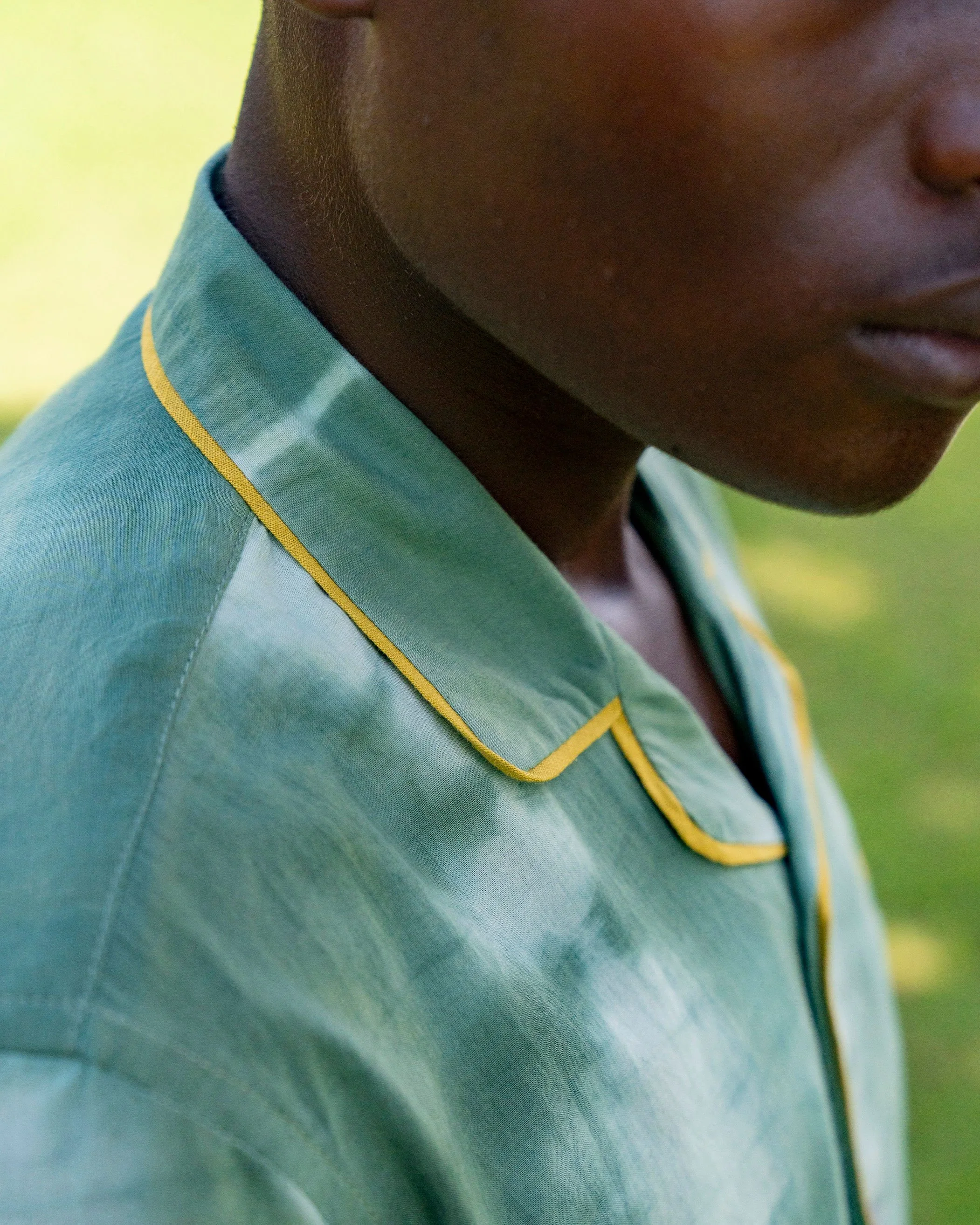 Close-up of a person with dark skin wearing a green shirt with yellow piping and a dark collar.