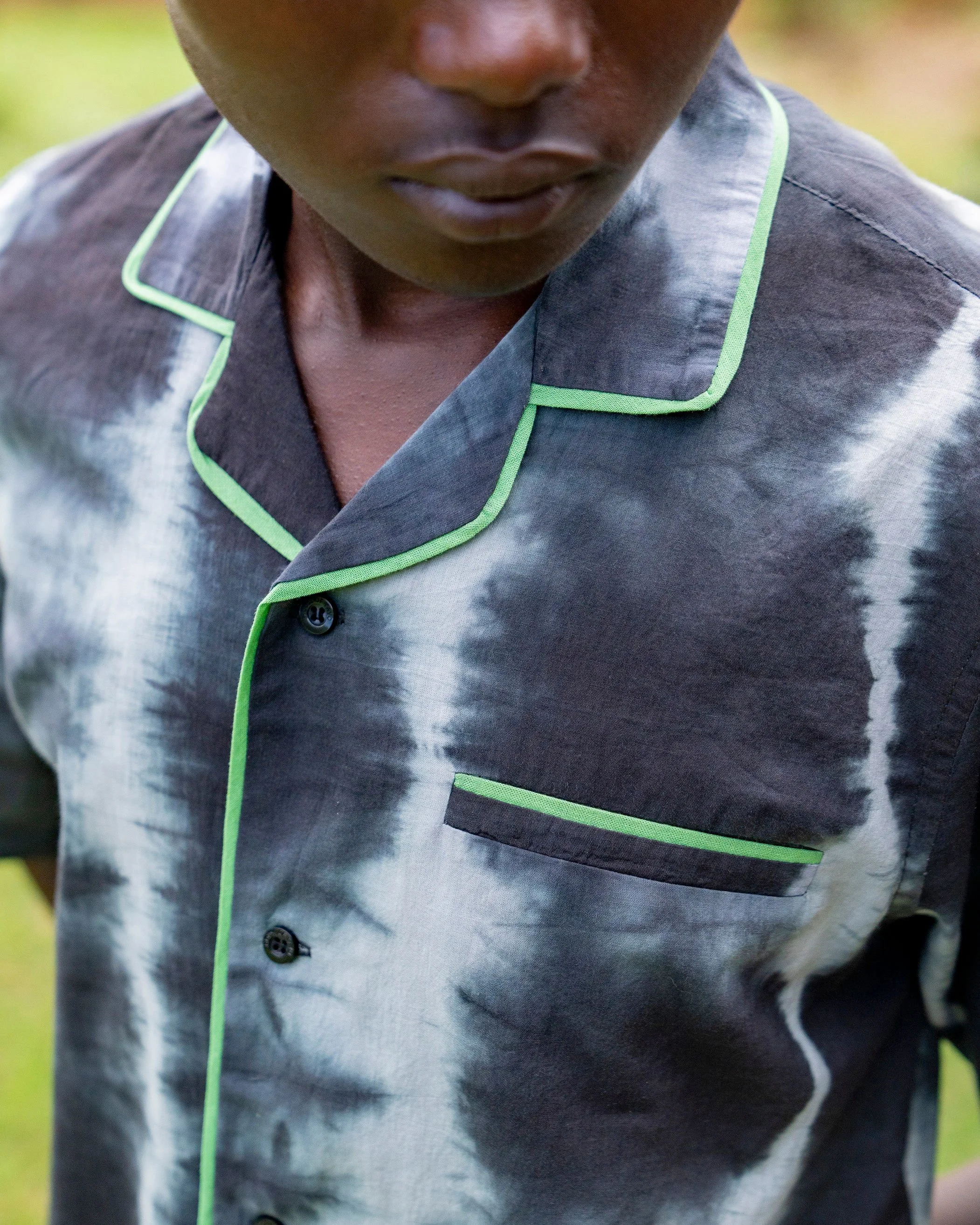 Close-up of a person wearing a grey shirt with green piping, showing the lower half of their face and part of the shirt's chest pocket.