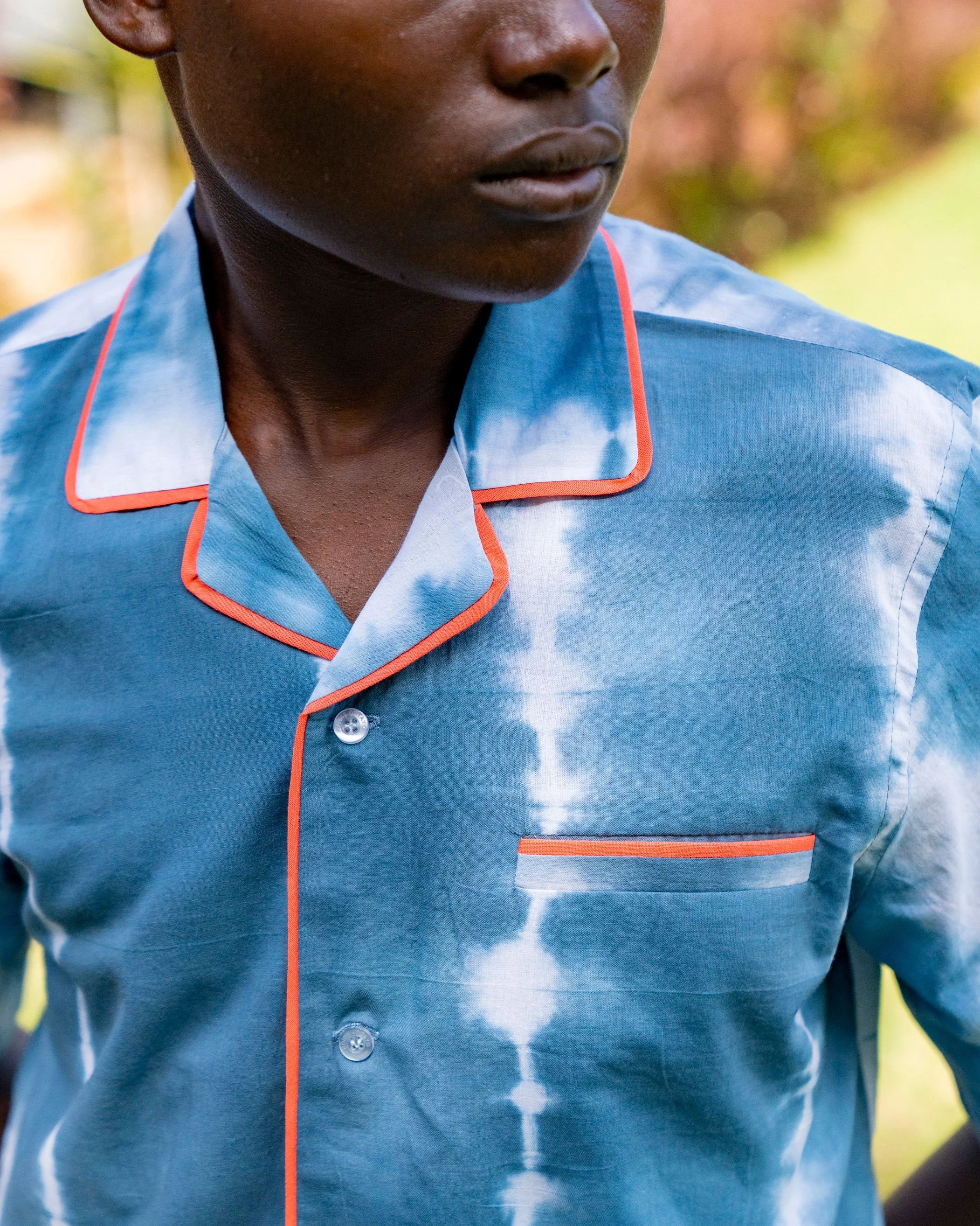 Close-up of a person with dark skin wearing a blue shirt with orange piping, with the focus on their chin, mouth, and collar area.