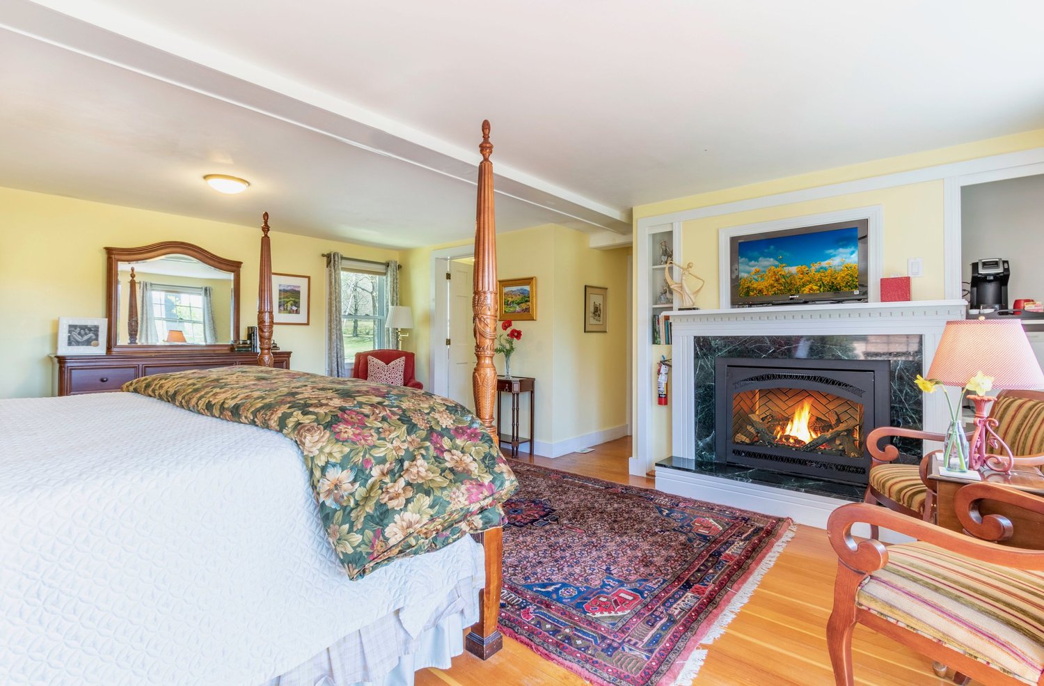 Cozy bedroom featuring a four-poster bed, fireplace, and a comfortable seating area with a colorful rug and warm decor.
